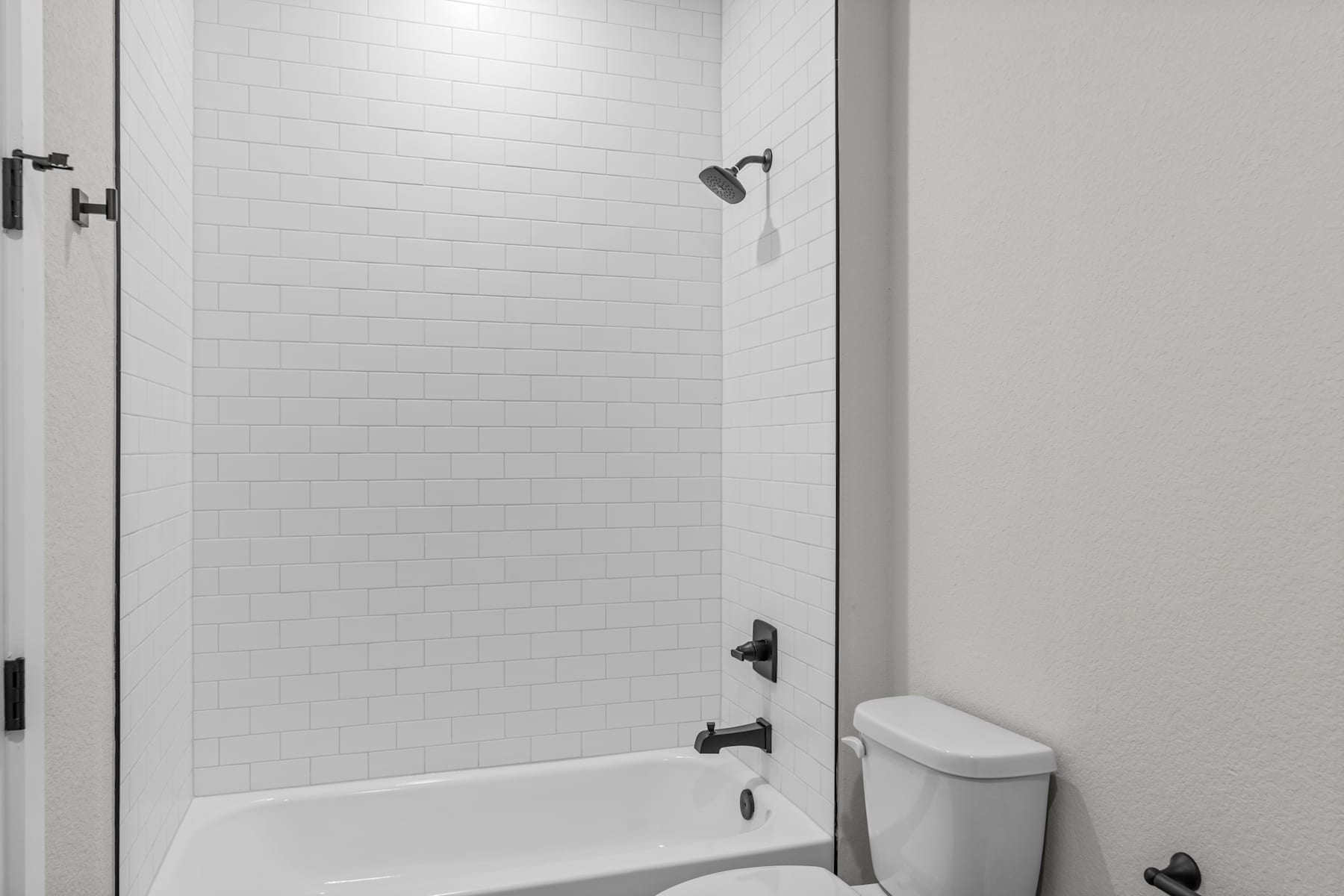 A modern, minimalist bathroom with a white tiled shower enclosure, a toilet, and a simple, clean design.