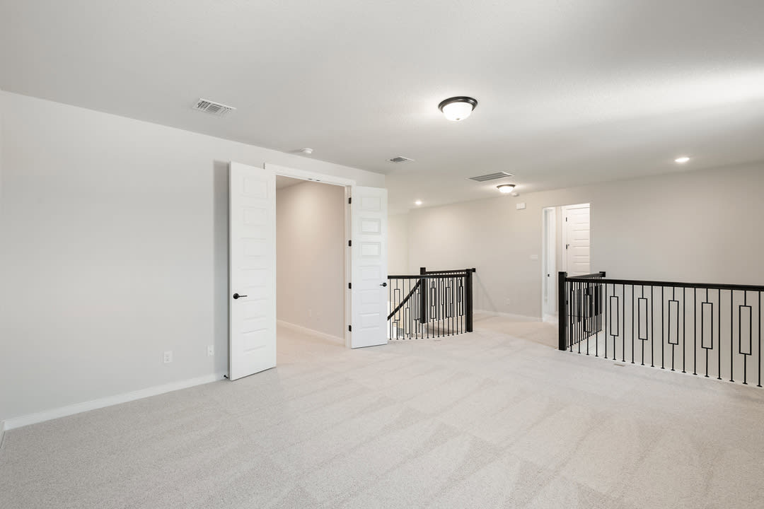 A spacious, well-lit hallway with white walls, a wooden floor, and a metal railing leading to a doorway.