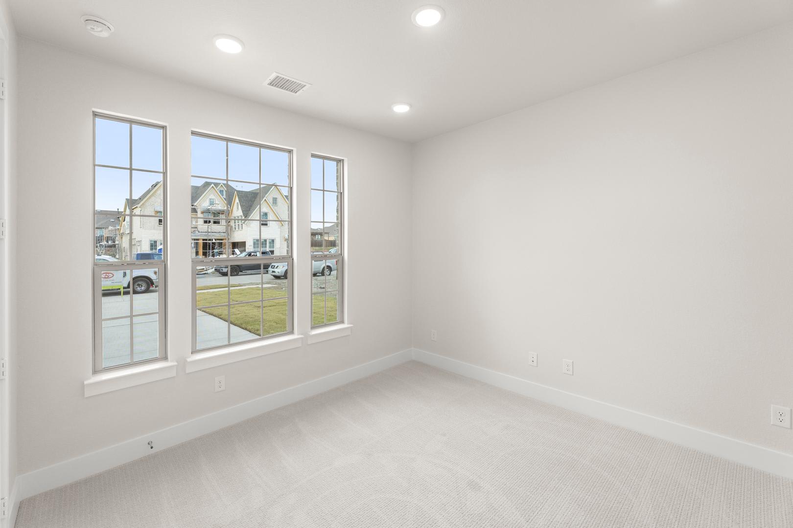 A bright, empty room with large windows overlooking a residential neighborhood in the background.