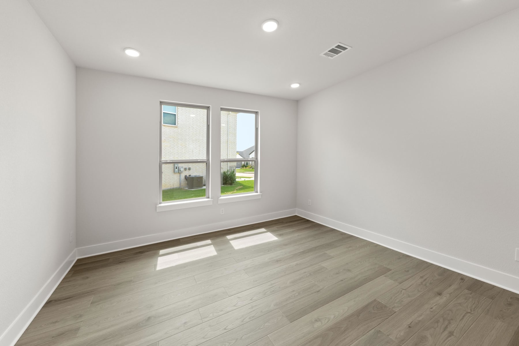 A spacious, well-lit room with a large window overlooking a grassy outdoor area, featuring a hardwood floor and neutral-toned walls.