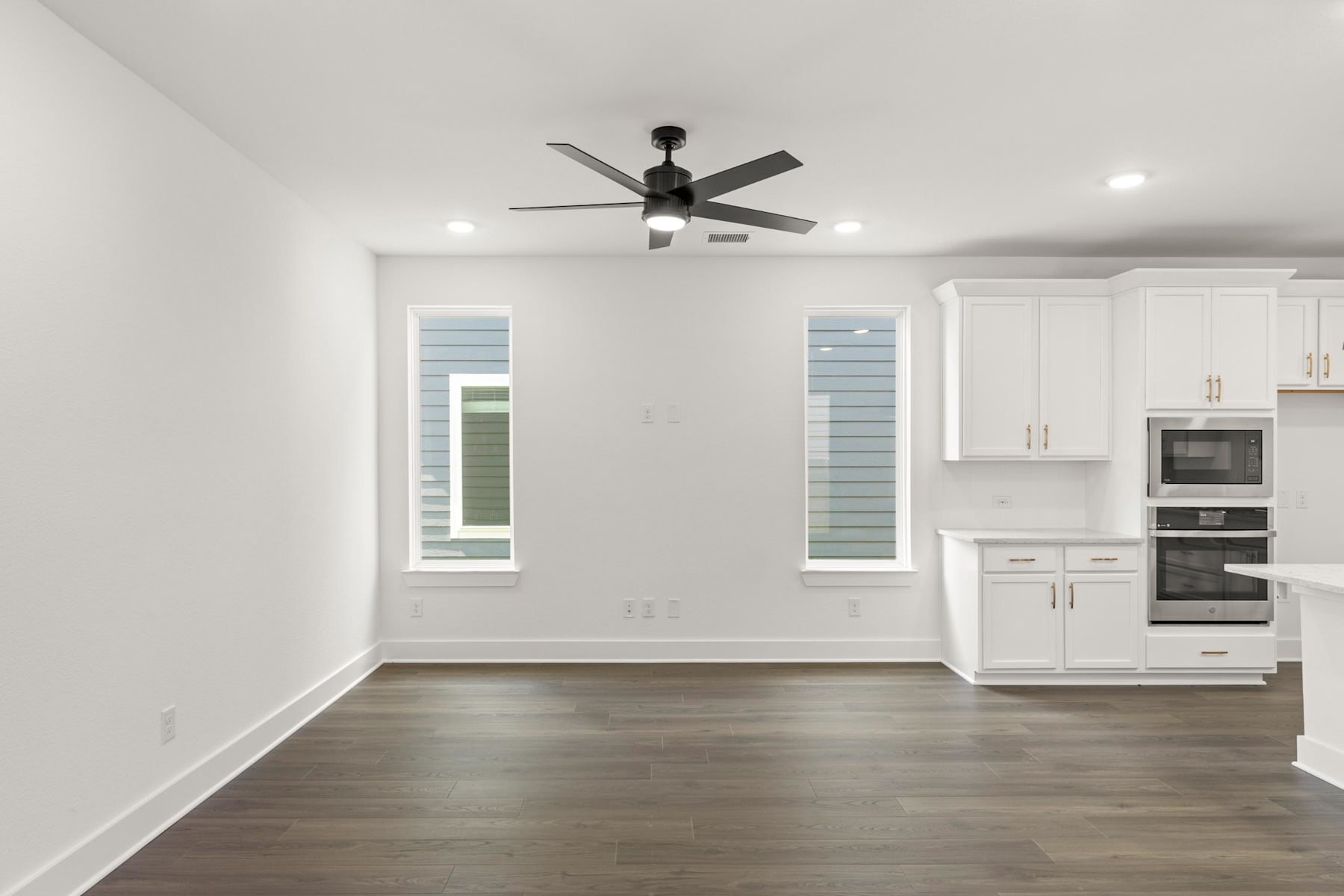 A modern, minimalist kitchen with white cabinets, a ceiling fan, and hardwood floors.