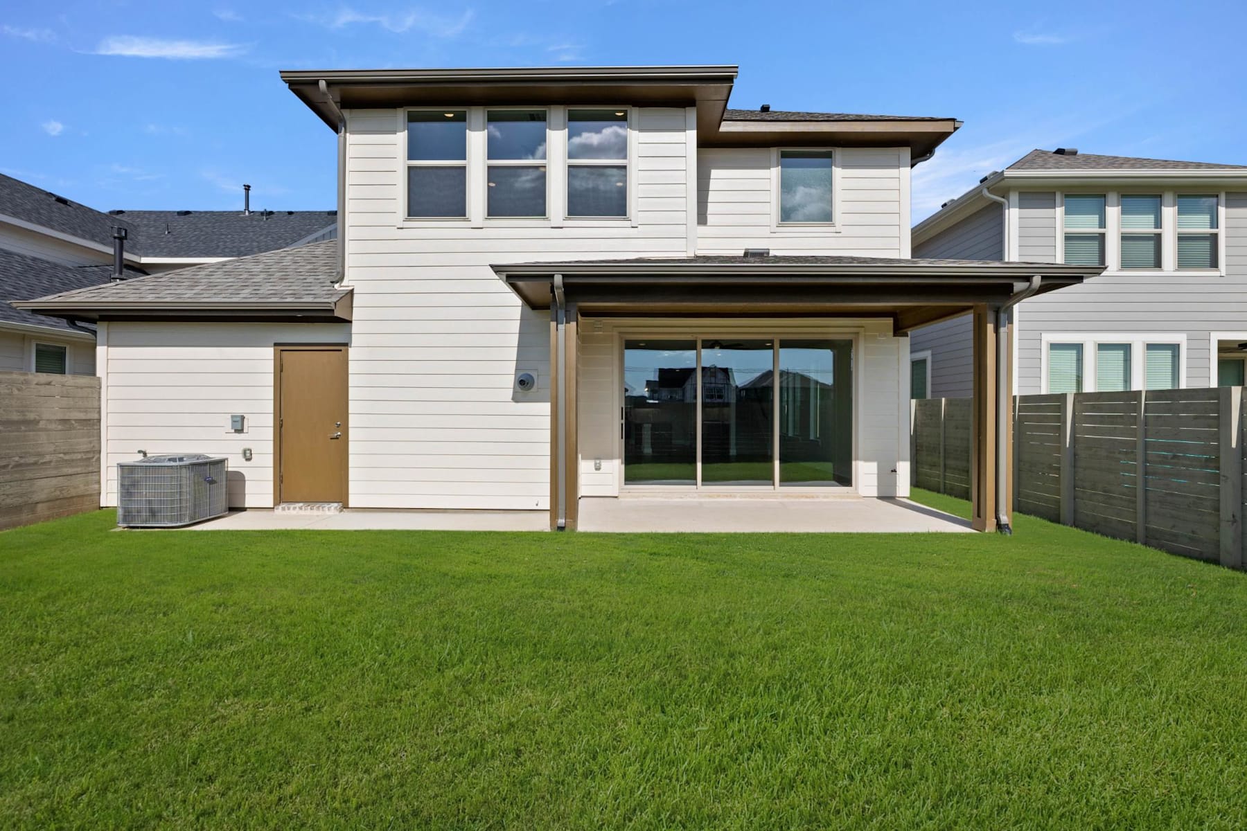 A modern two-story house with a well-manicured lawn in the foreground, set against a clear blue sky in the background.