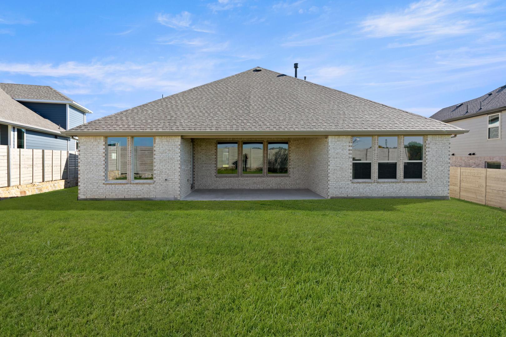 A single-story house with a gray roof and exterior walls, surrounded by a lush green lawn, set against a clear blue sky with scattered clouds.