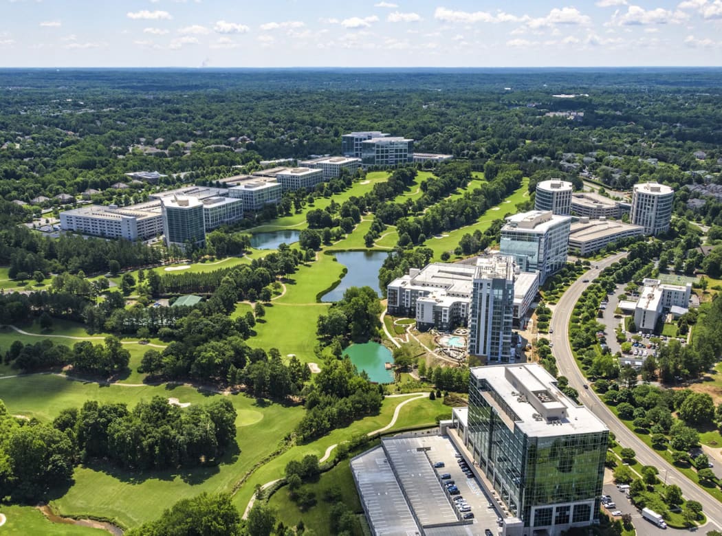 A sprawling urban landscape with towering buildings, lush green spaces, and winding waterways, set against a backdrop of a clear blue sky with scattered clouds.