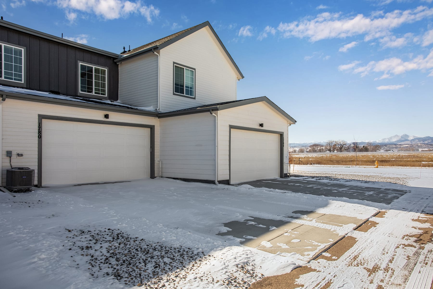 A two-story residential building with a garage and a snowy driveway, set against a backdrop of a cloudy blue sky.