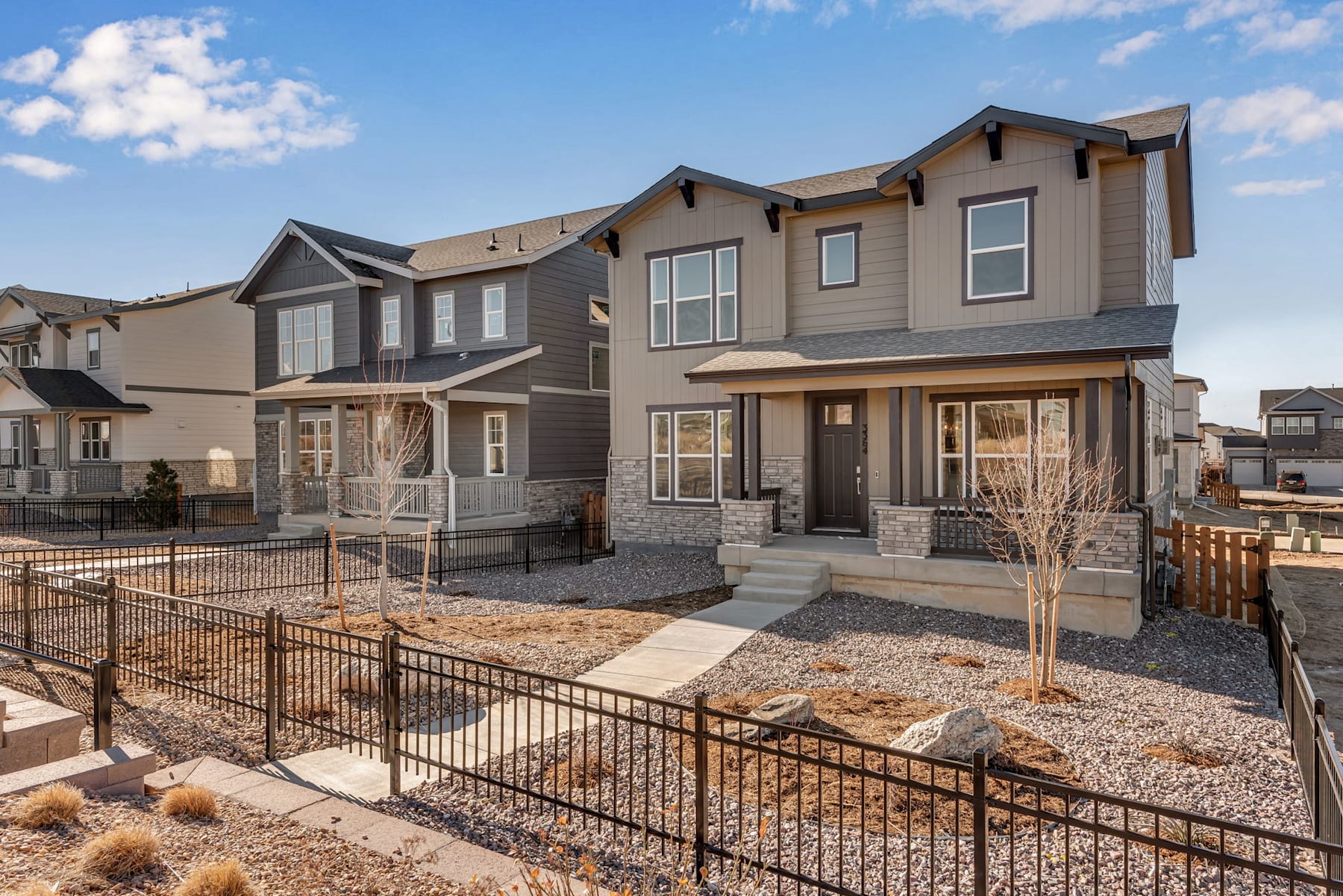A residential neighborhood with multi-story townhouses, featuring a fenced-in yard in the foreground and a clear blue sky with scattered clouds in the background.