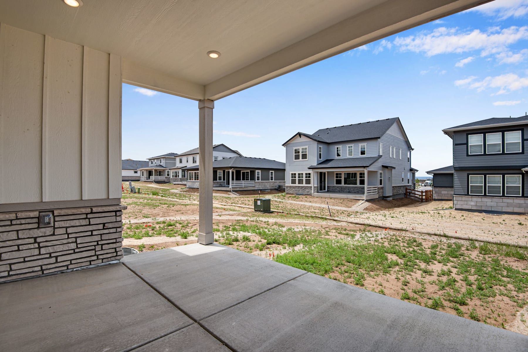 The image shows a residential neighborhood with newly constructed houses, a paved walkway in the foreground, and a grassy area surrounding the homes.