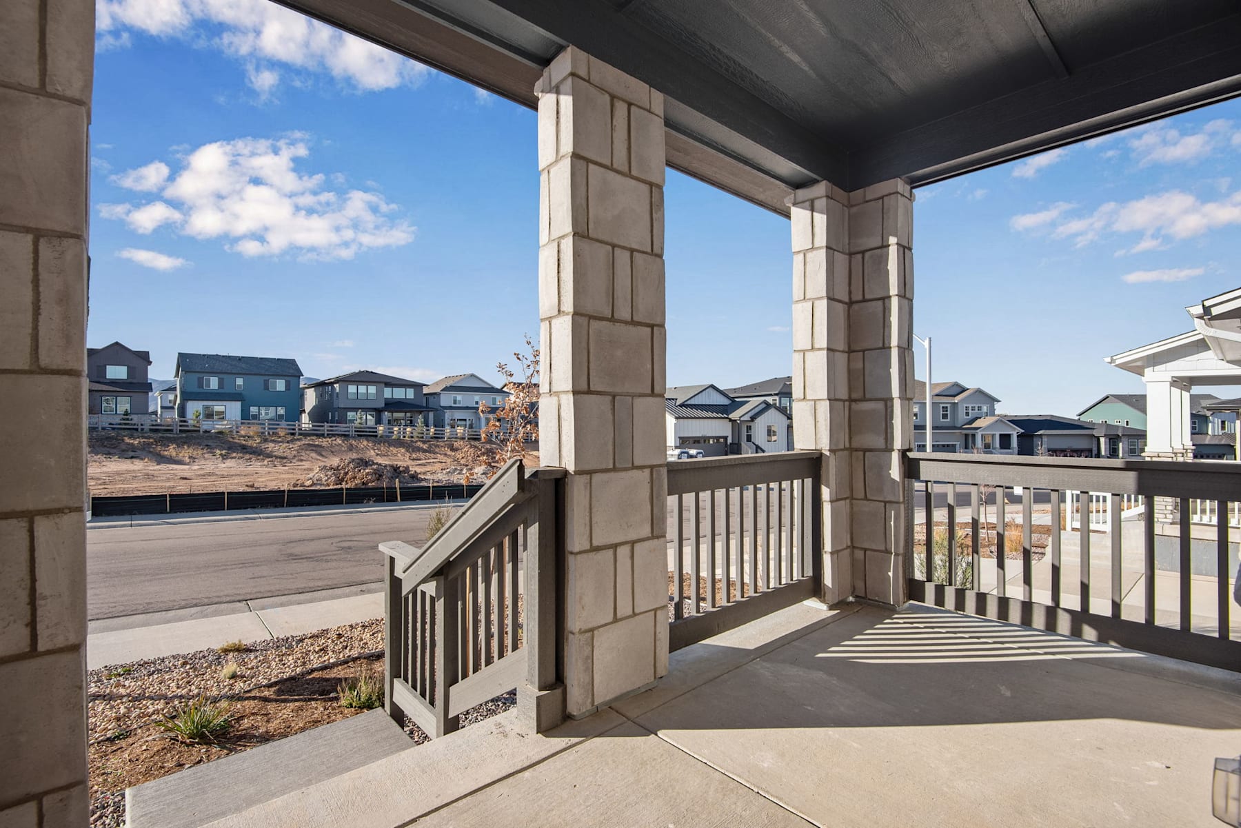 A covered porch with a railing overlooks a residential neighborhood with houses and buildings in the background under a cloudy sky.