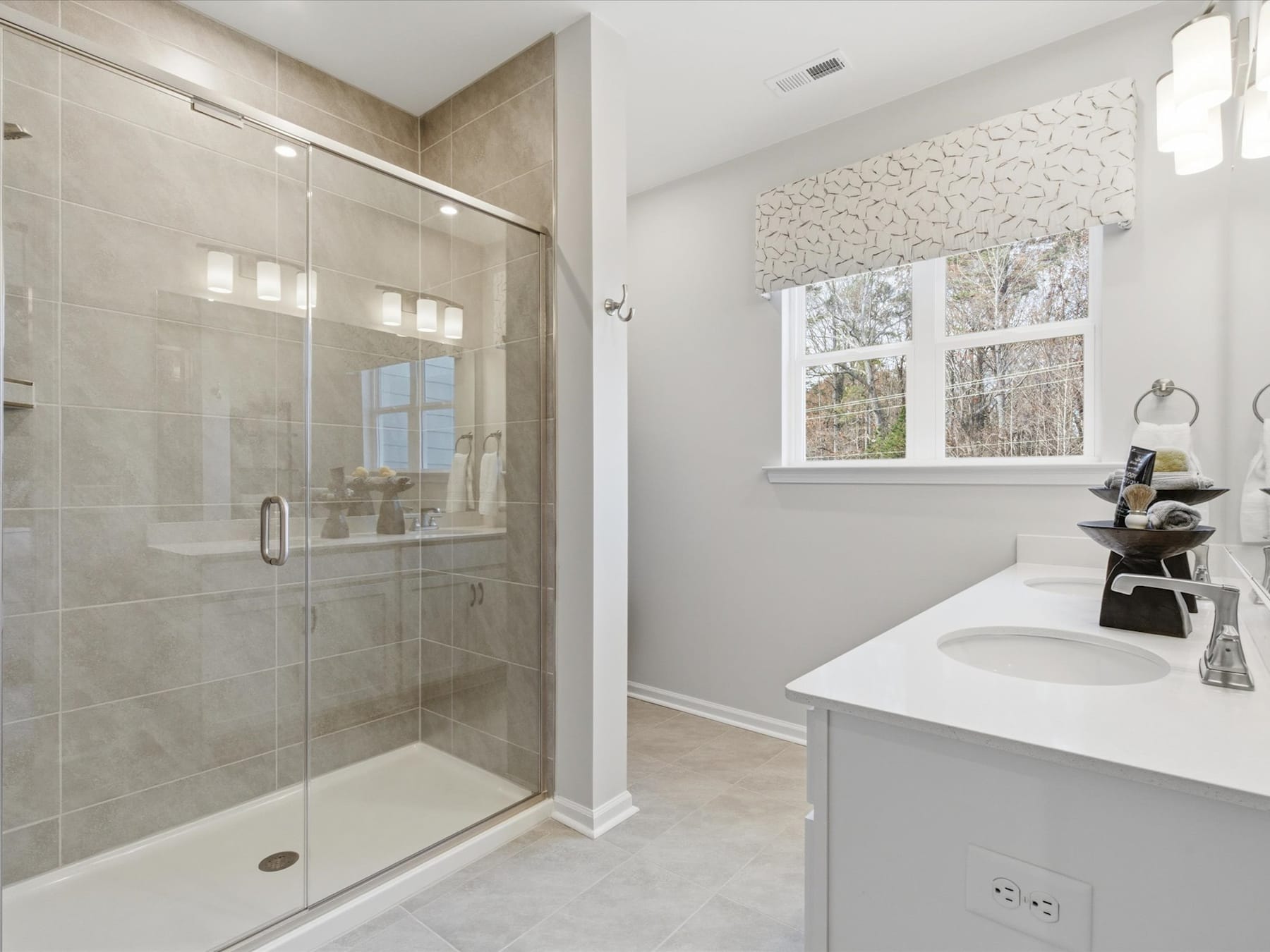 A modern, well-lit bathroom with a large glass shower enclosure, a white vanity, and a window overlooking the outdoors.