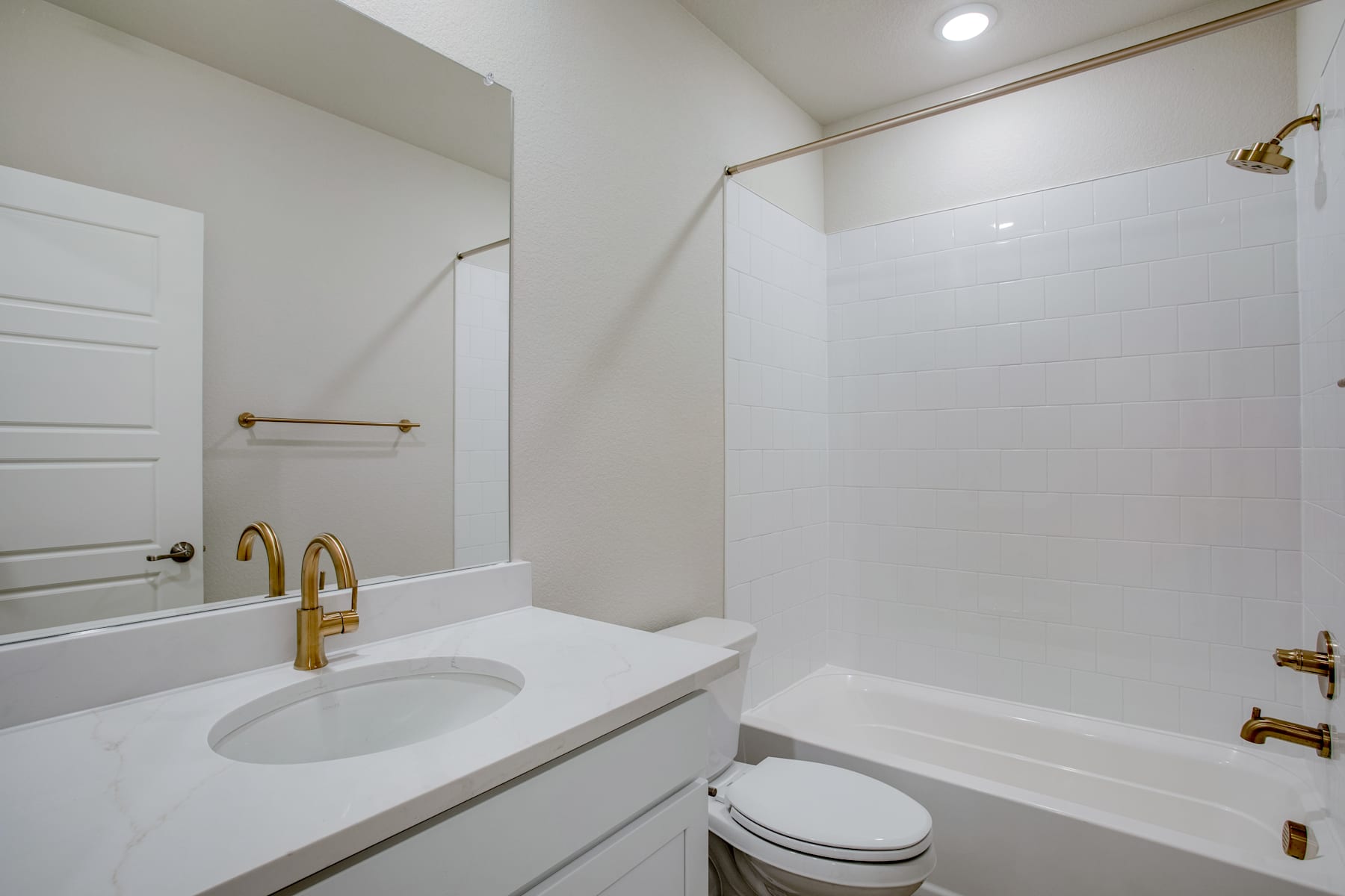 A modern, minimalist bathroom with a white vanity, sink, and toilet, along with gold-colored fixtures and accents.