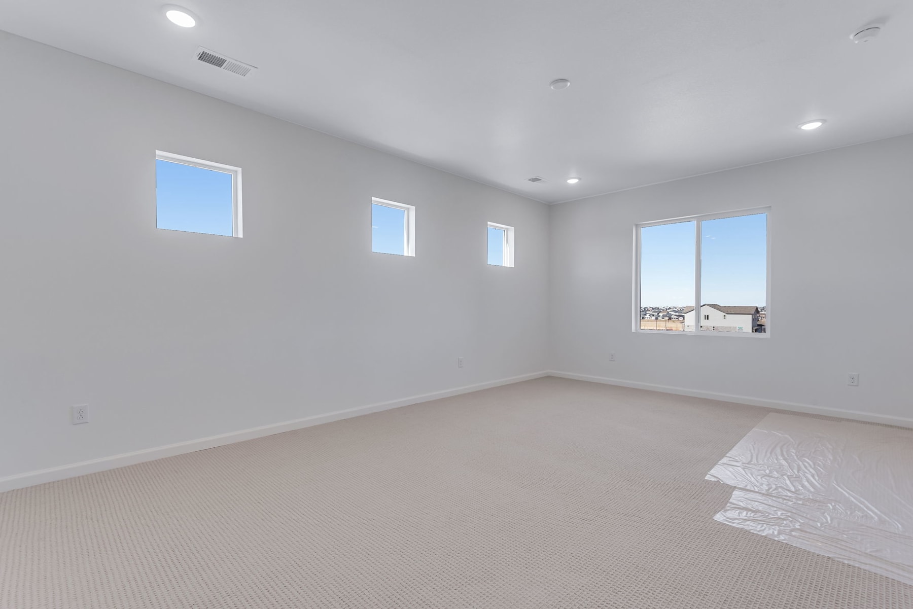 A spacious, well-lit room with white walls, a carpeted floor, and several windows providing natural light.