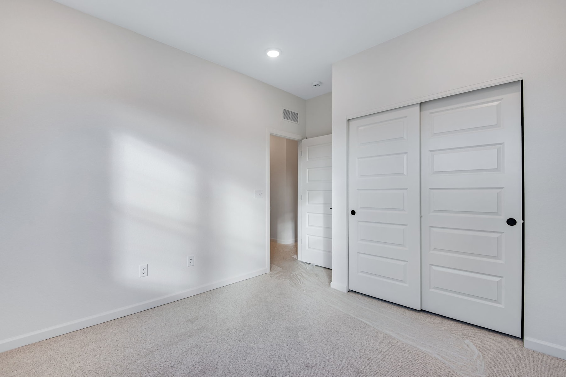 A spacious, minimalist room with white walls, a hardwood floor, and two white sliding doors in the background.