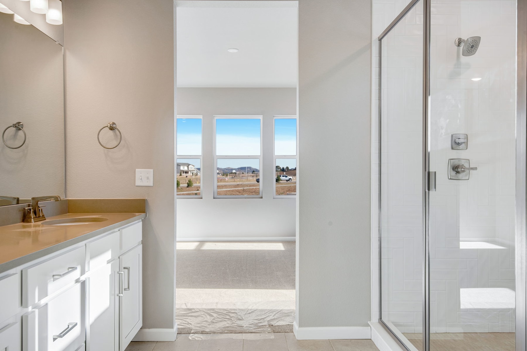 A modern, well-lit bathroom with a vanity, shower, and large windows overlooking a scenic outdoor view.