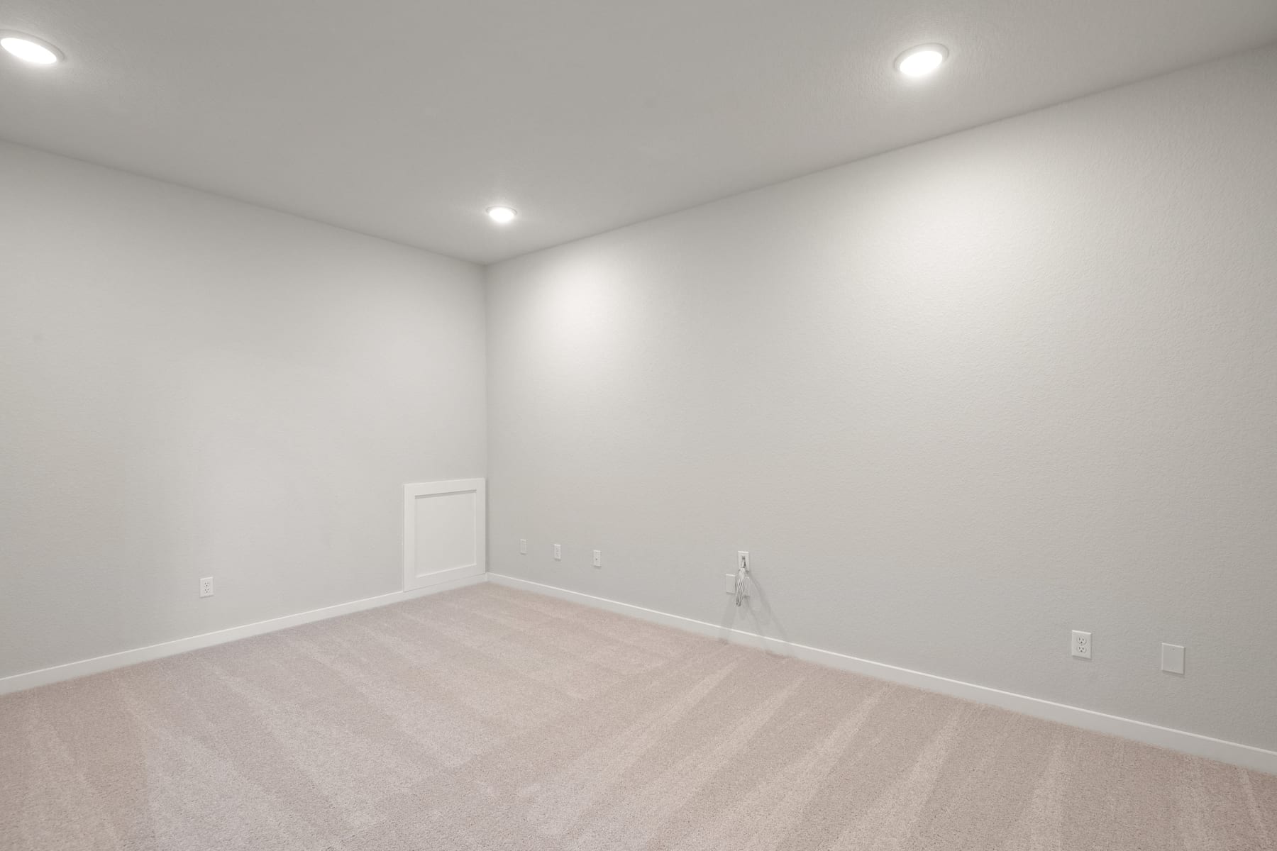 A spacious, well-lit room with white walls and a light-colored hardwood floor, featuring a single door in the background.