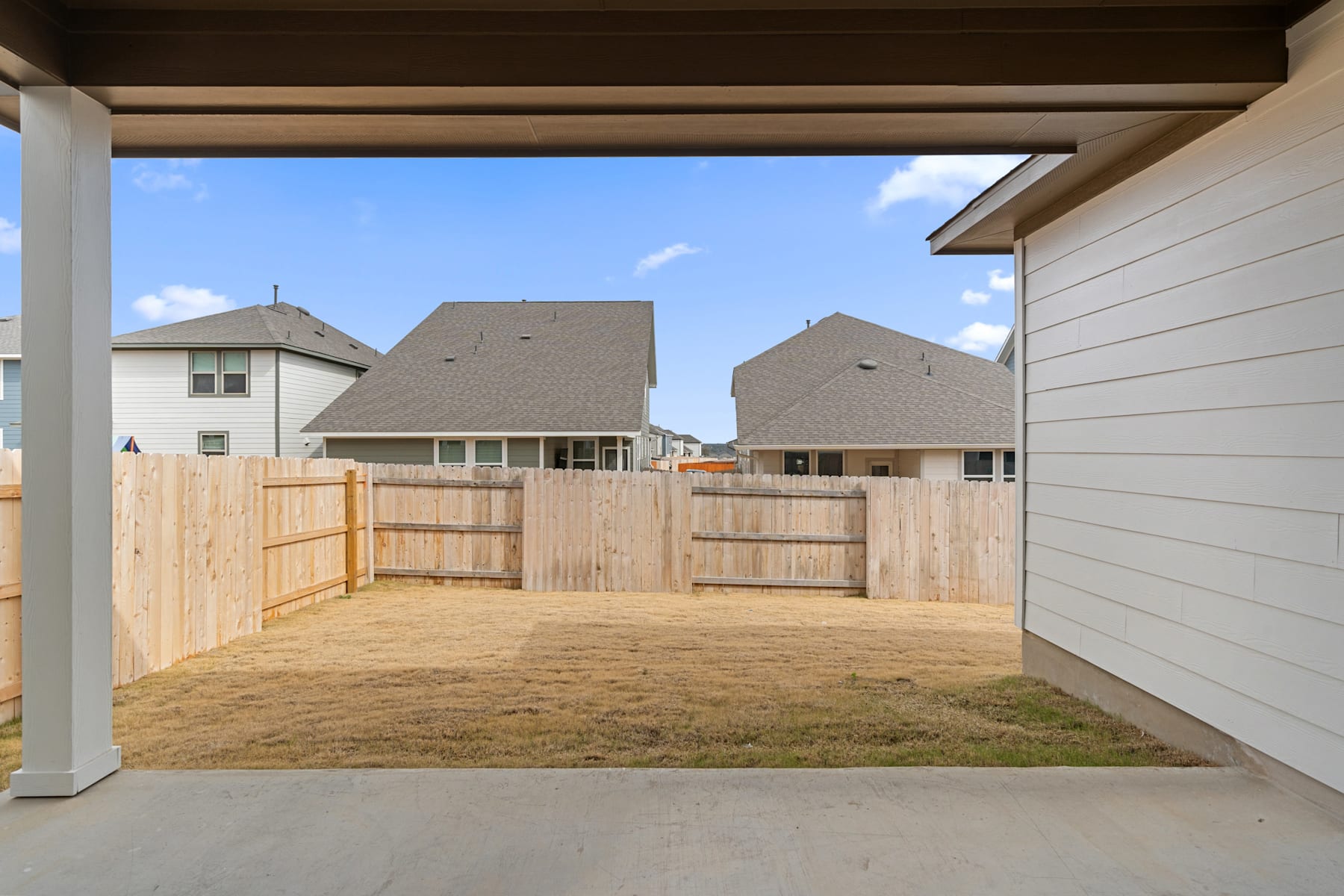 A wooden fence surrounds a grassy yard, with several houses visible in the background under a clear blue sky.