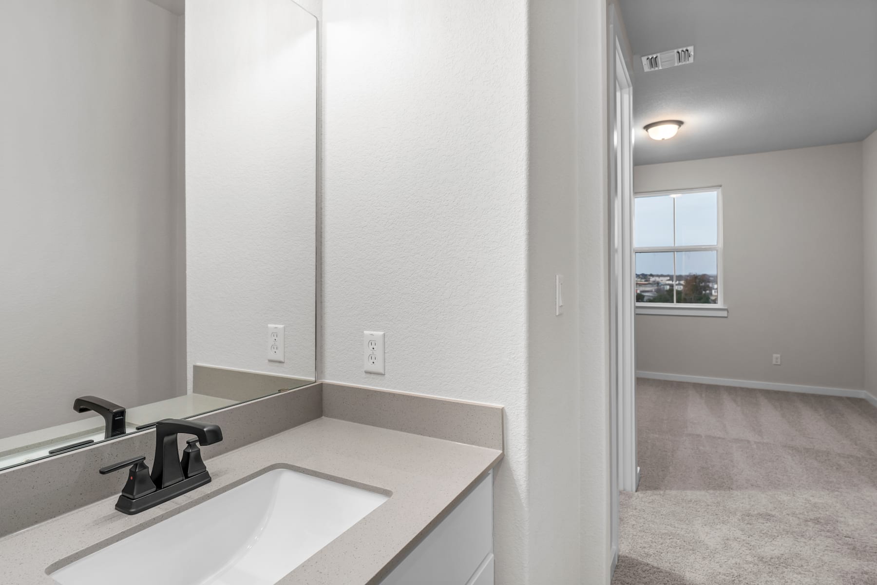 A modern, minimalist bathroom with a white vanity, a large mirror, and a window providing natural light.
