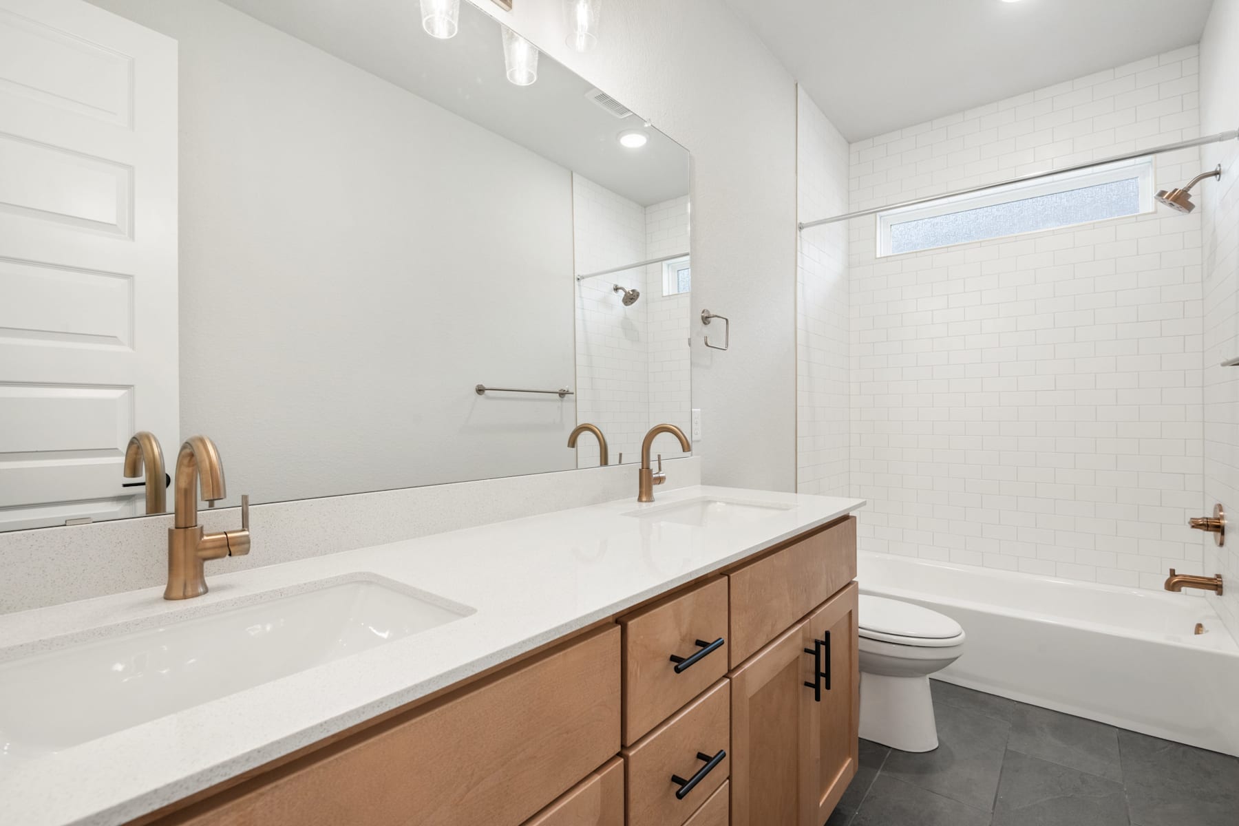 A modern, minimalist bathroom with a white countertop, wooden cabinets, and a toilet in the background.