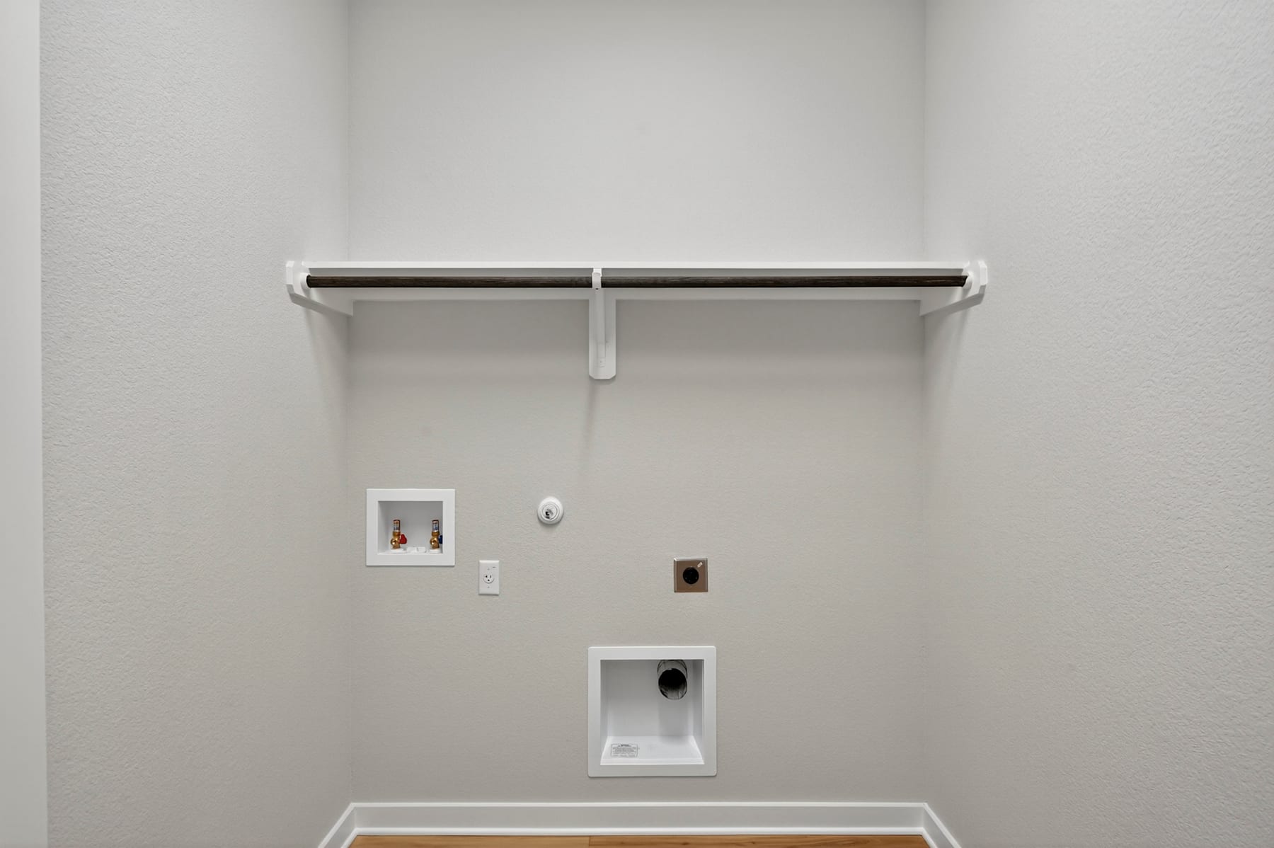 A simple, minimalist wall with a white shelf, electrical outlets, and a small framed artwork.