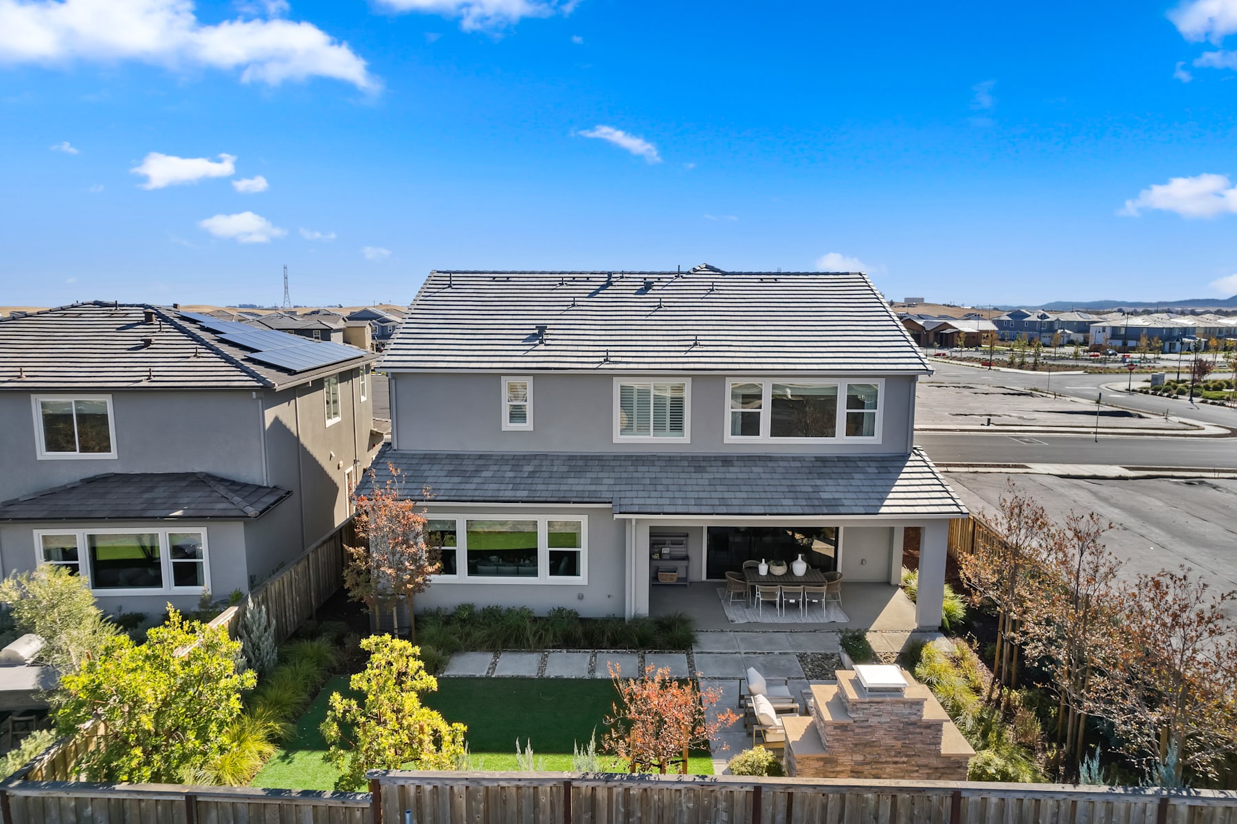 A two-story residential building with a gray exterior and a slanted roof, surrounded by a well-maintained yard with various plants and a paved walkway leading to the entrance.