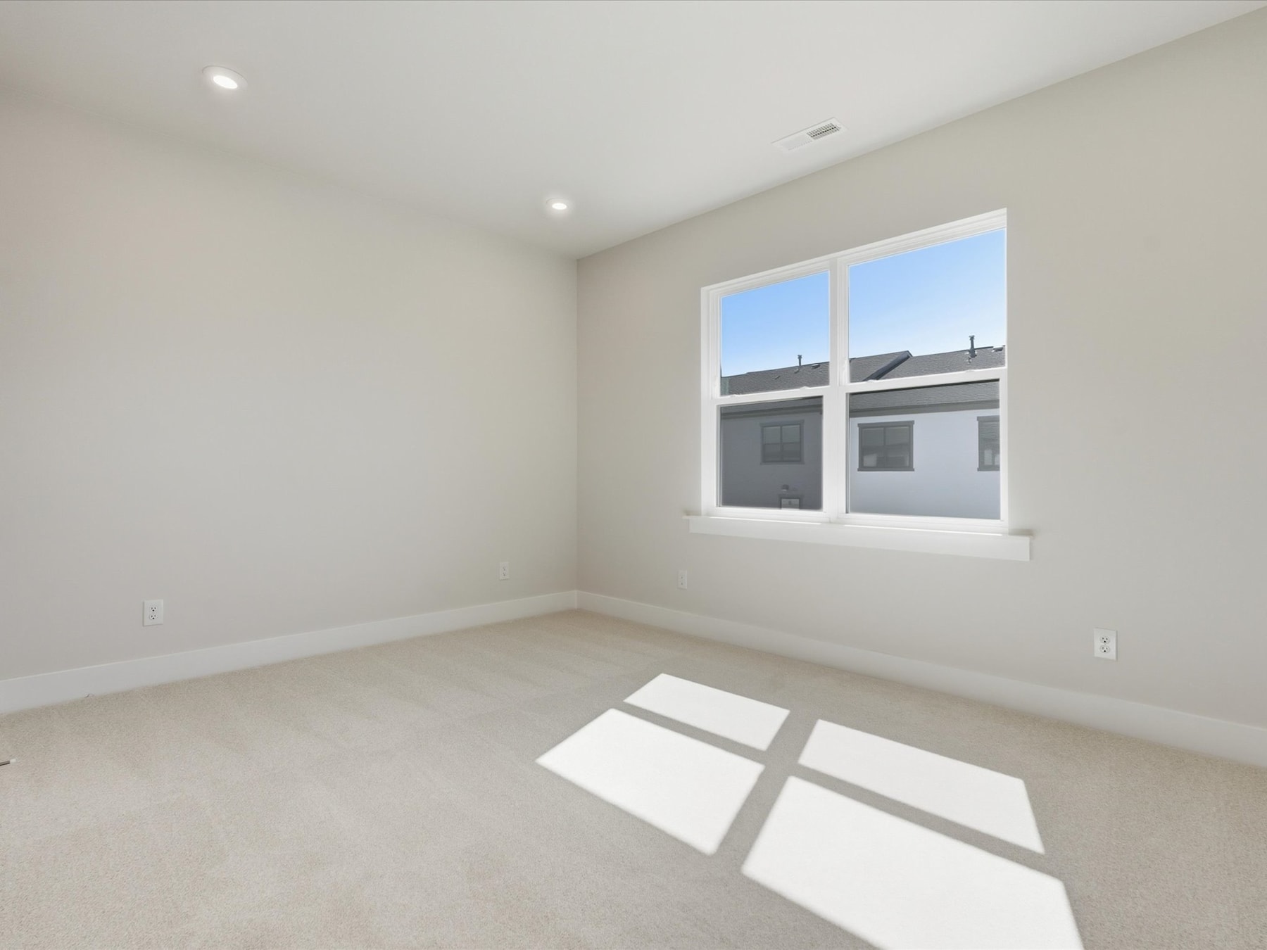 A bright, empty room with a large window letting in natural light, casting shadows on the plain white walls and floor.
