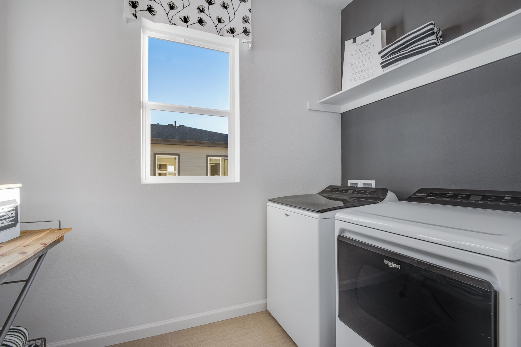 A bright and airy laundry room with a large window, shelves, and a washer and dryer set against a gray wall.