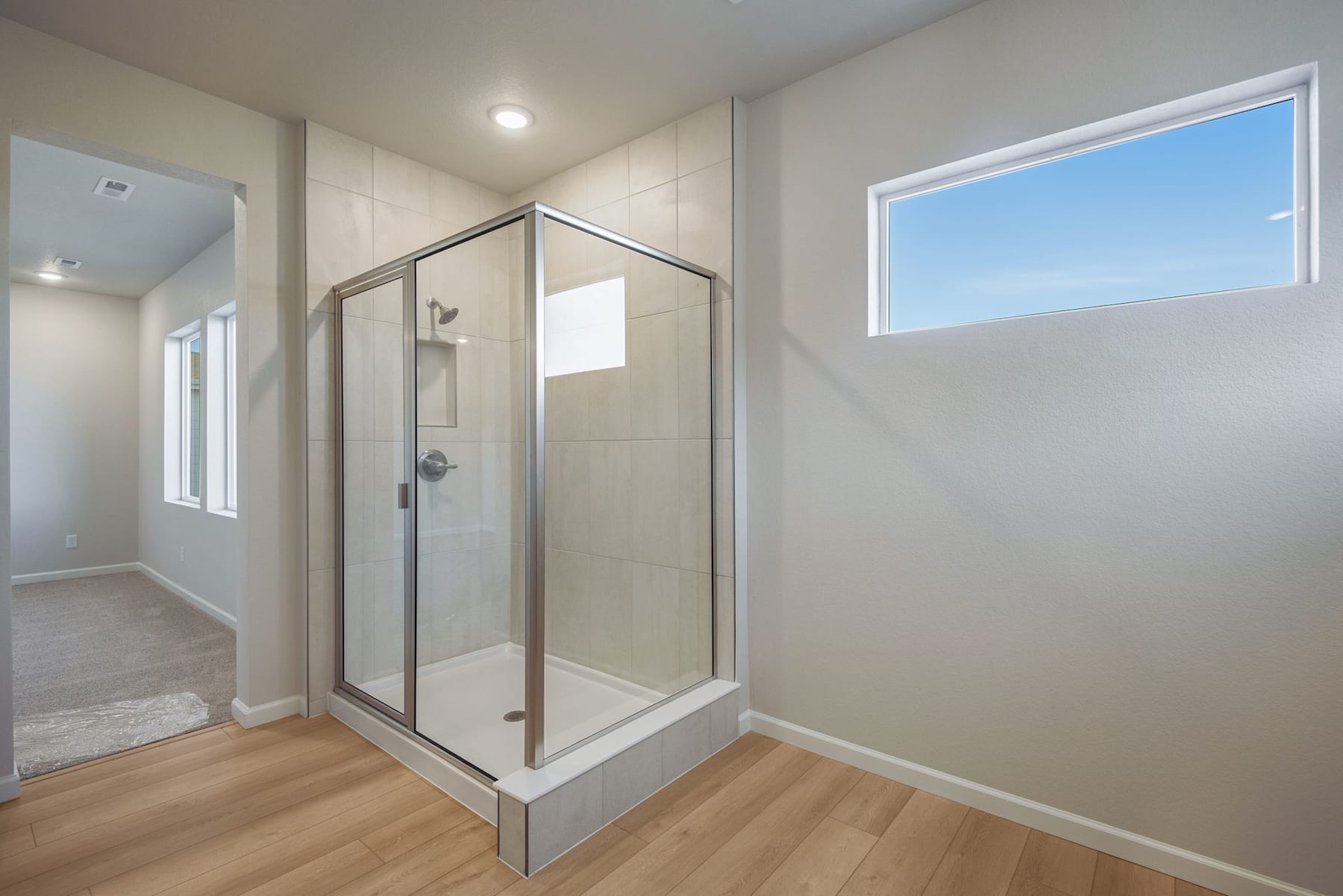 A modern bathroom with a glass-enclosed shower, hardwood flooring, and a window providing natural light.