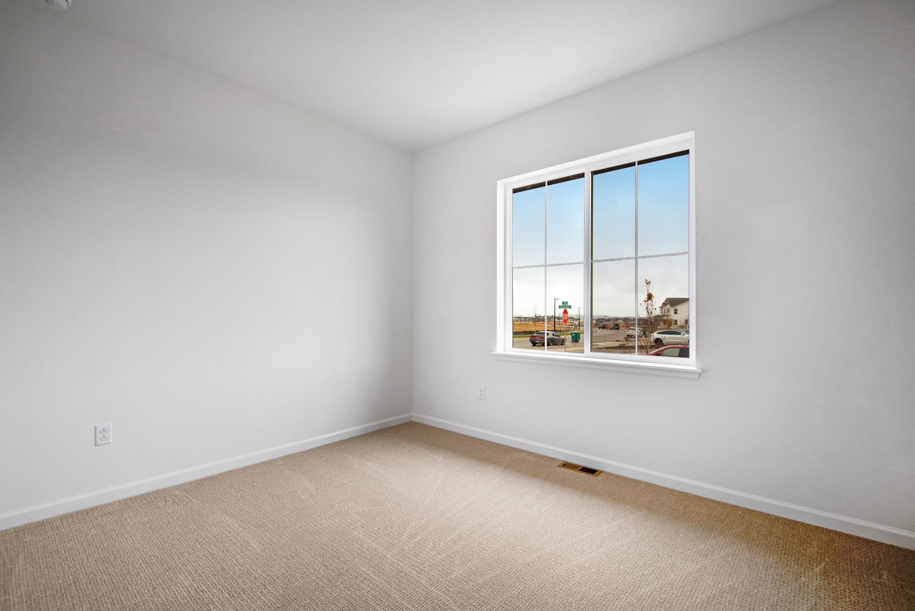 A bright, empty room with a large window overlooking a residential area in the background.