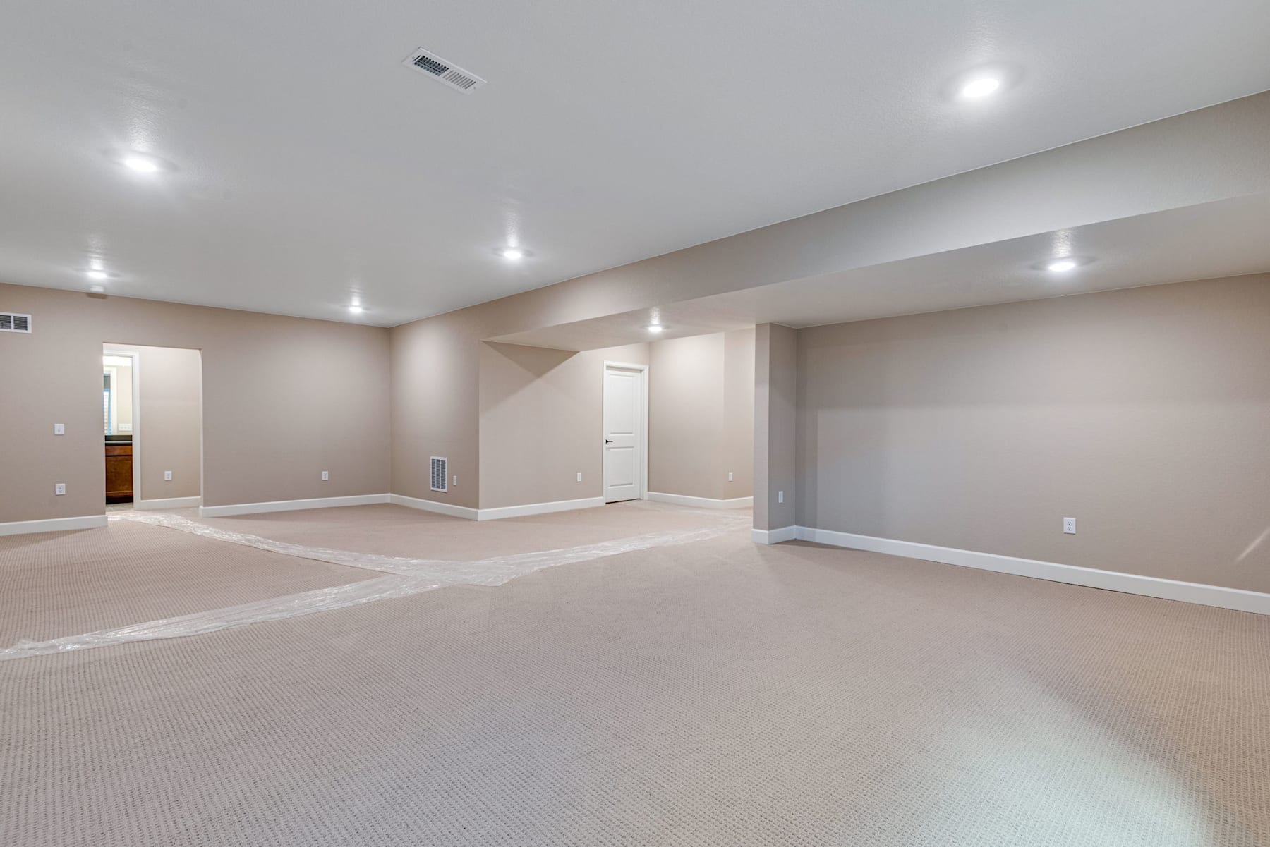 A spacious, well-lit room with beige walls, recessed lighting, and a carpeted floor, creating a clean and inviting atmosphere.