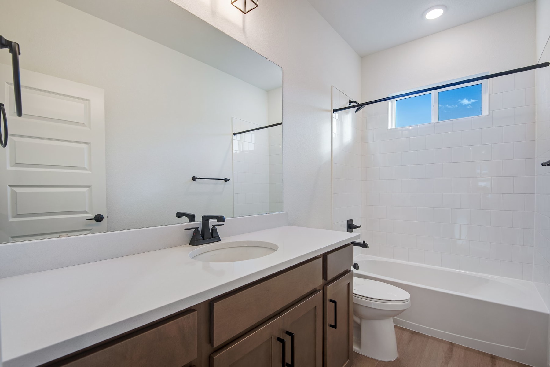 A modern and clean bathroom with a white vanity, a large mirror, and a window providing natural light.