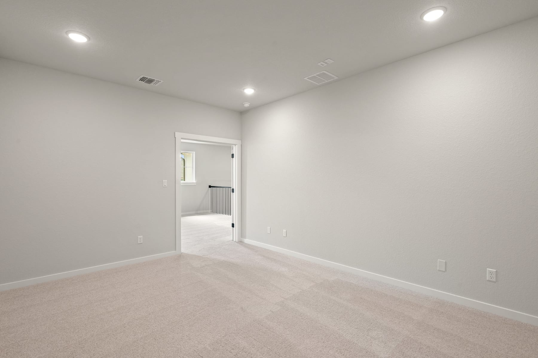 A spacious, well-lit room with a neutral color scheme and recessed lighting, featuring a doorway leading to another room.