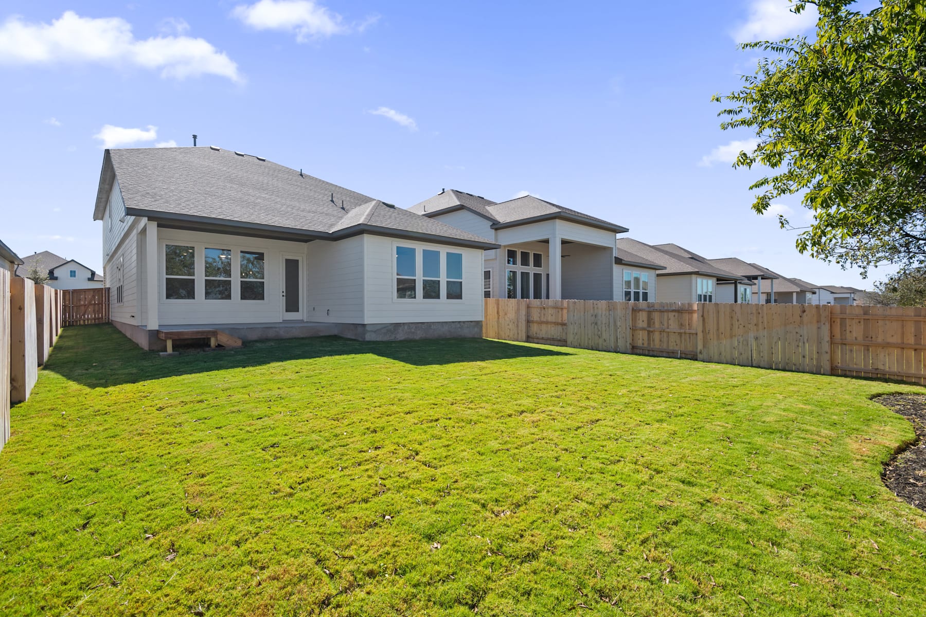 A well-manicured lawn surrounds a modern, multi-story residential building with a gray roof and large windows, set against a clear blue sky with scattered clouds.