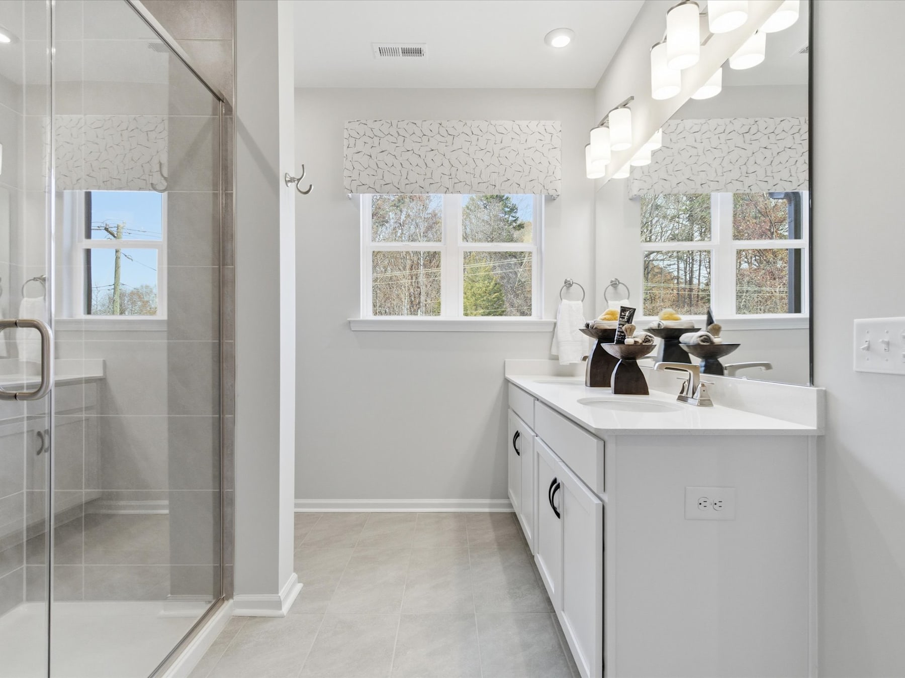 A modern, well-lit bathroom with a white vanity, a glass shower enclosure, and decorative lighting fixtures on the ceiling.