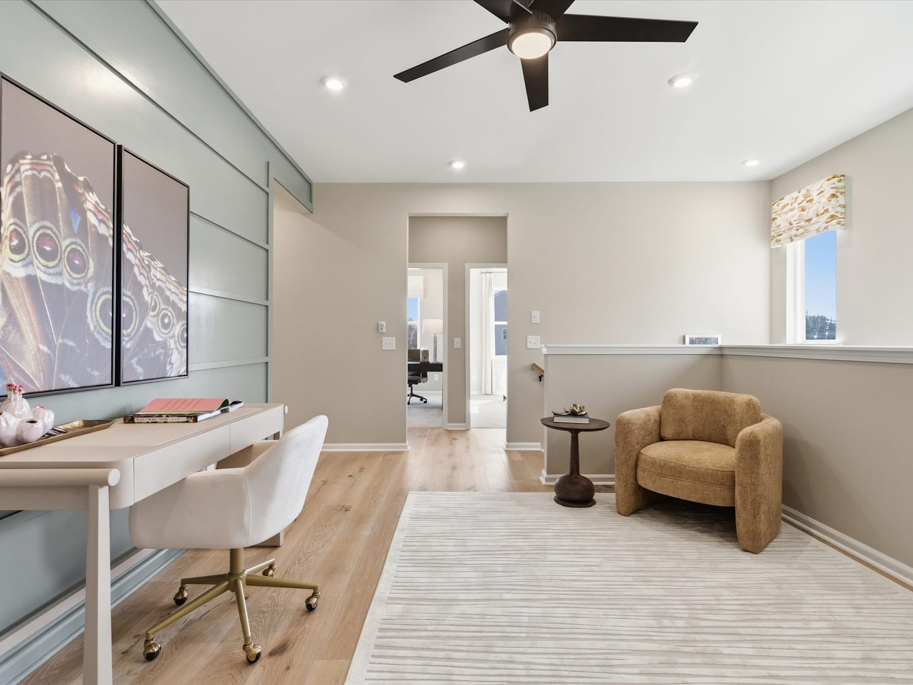 A modern and well-furnished home office space with a comfortable armchair, a desk, and a ceiling fan, set against a neutral-toned background.