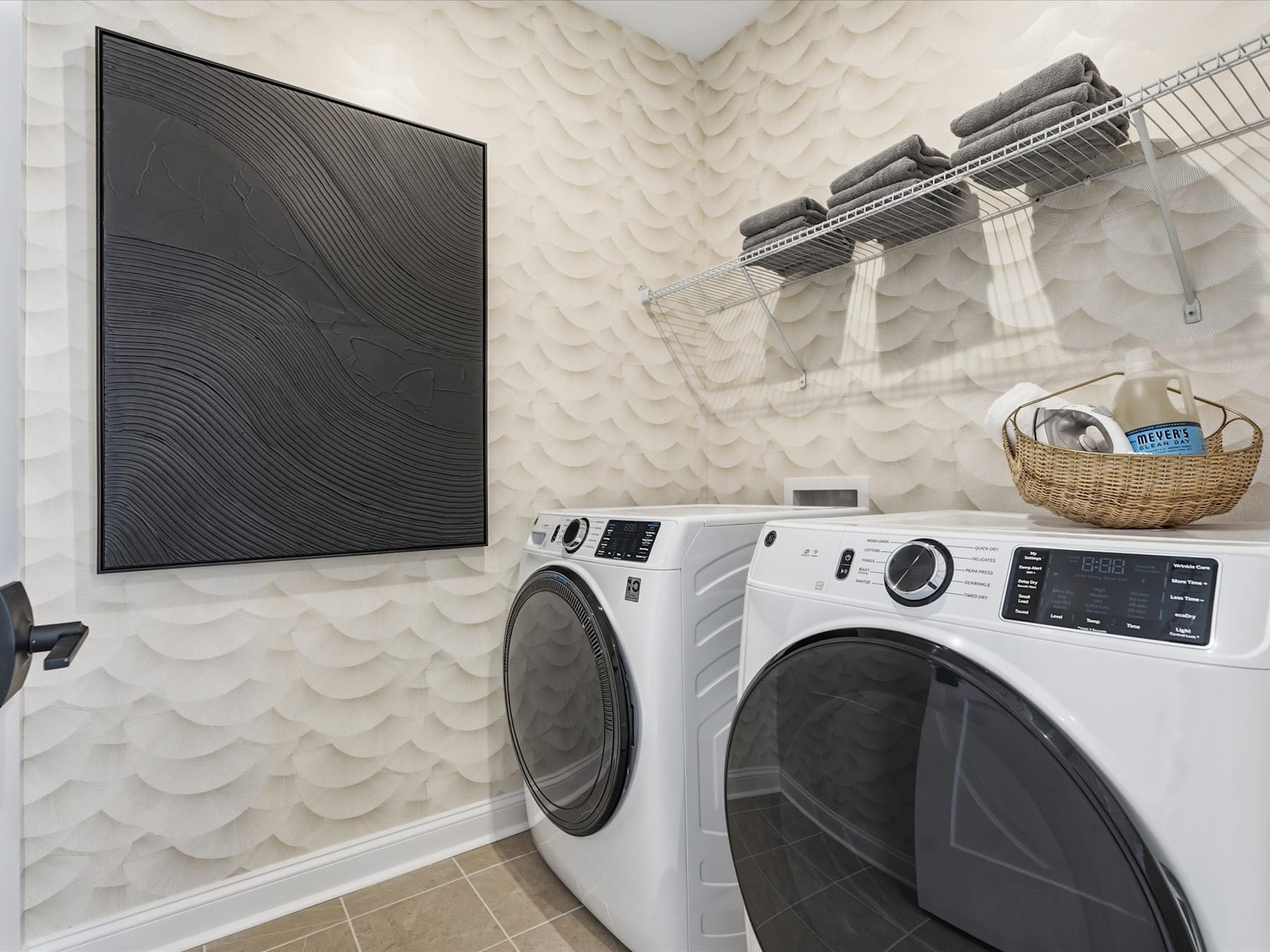 A modern and minimalist laundry room with a large black abstract artwork, a white washer and dryer, and various storage and organizational elements.