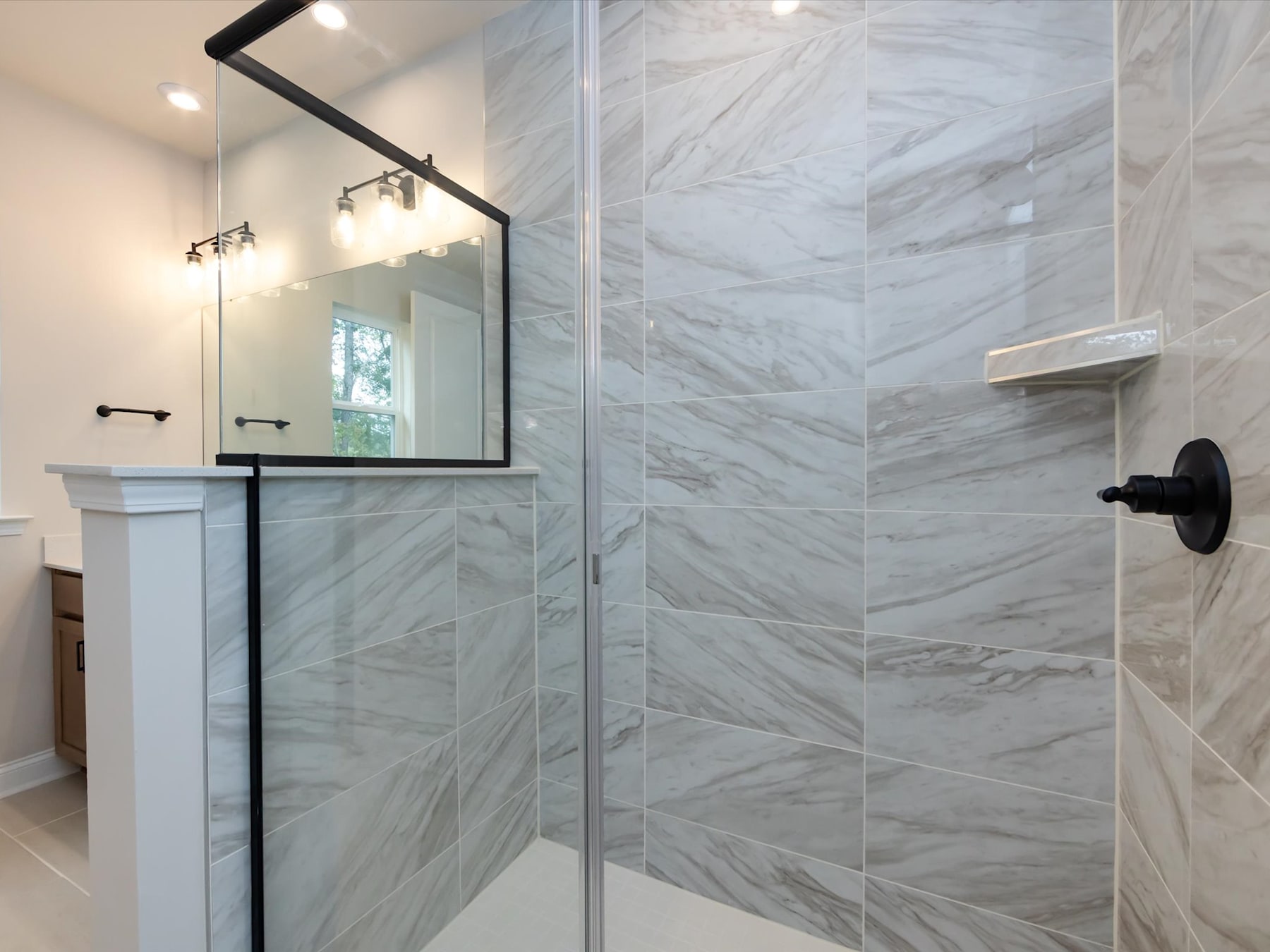 A modern and elegant bathroom with a large mirror, a vanity, and a spacious shower enclosure with marble-like tiles covering the walls.