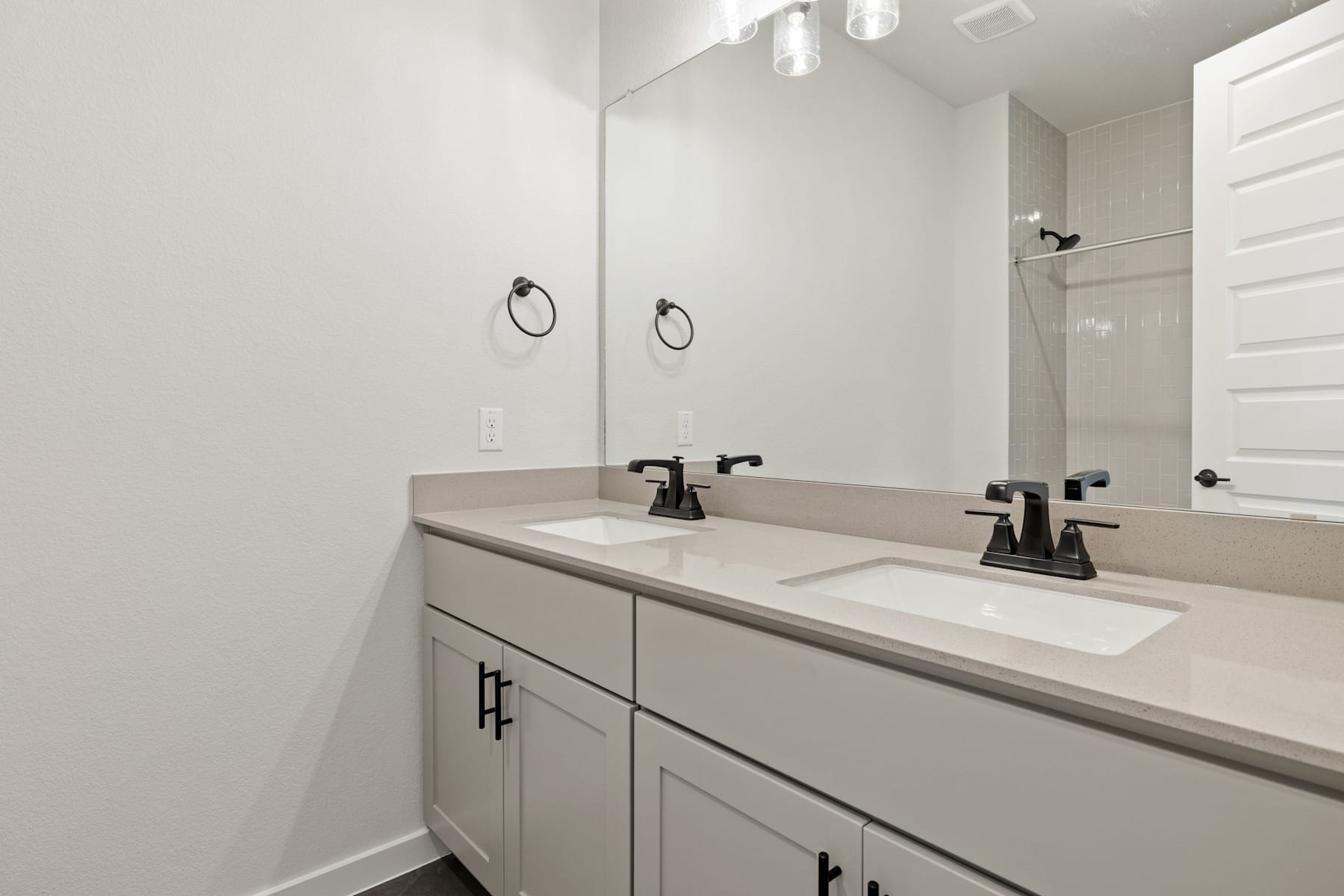 A modern bathroom with a double vanity, white countertop, and black faucets, set against a plain white wall background.
