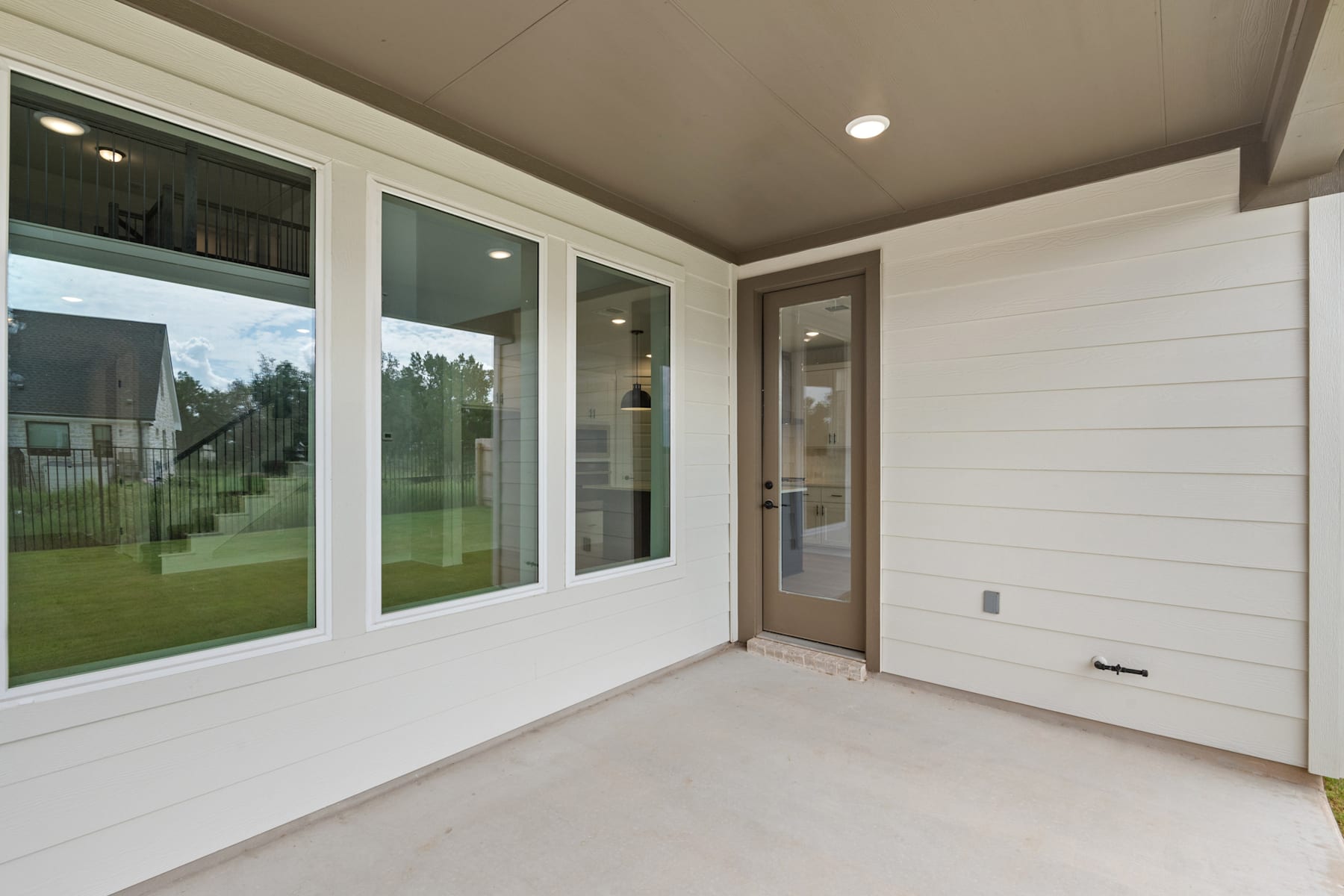 A bright and airy interior space with large windows overlooking a grassy outdoor area, featuring a wooden door and white shiplap walls.