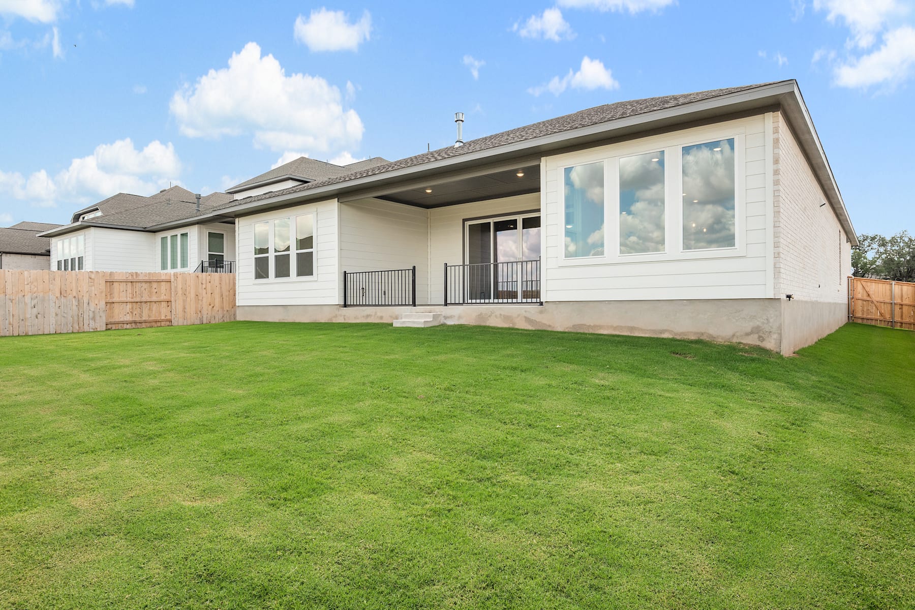 A modern, single-story house with a large grassy yard in the foreground, set against a blue sky with fluffy white clouds.