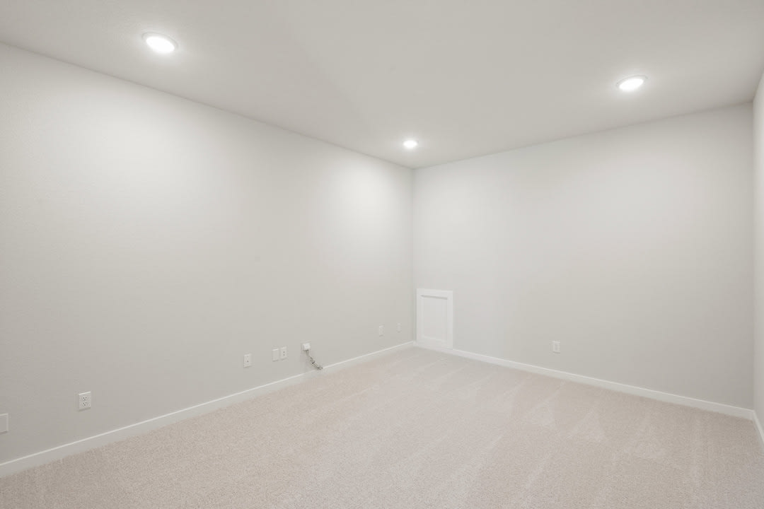 A bright, empty room with white walls and a light-colored floor, illuminated by recessed ceiling lights.