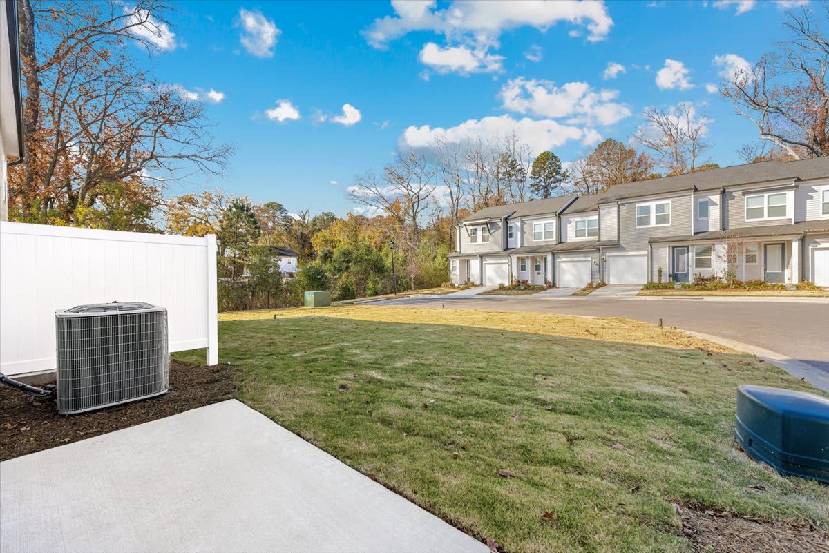 The image shows a residential neighborhood with townhouses, a well-manicured lawn, and a clear blue sky with fluffy white clouds.
