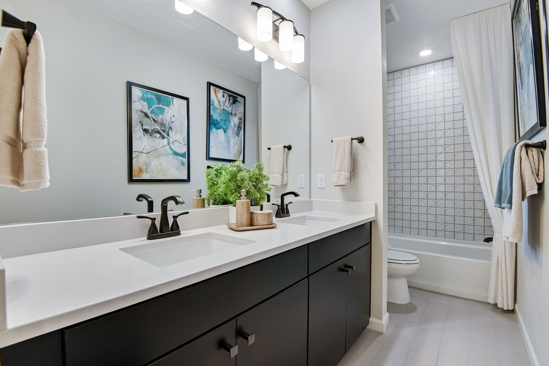 A modern and stylish bathroom with a double vanity, black cabinets, and abstract artwork on the walls.