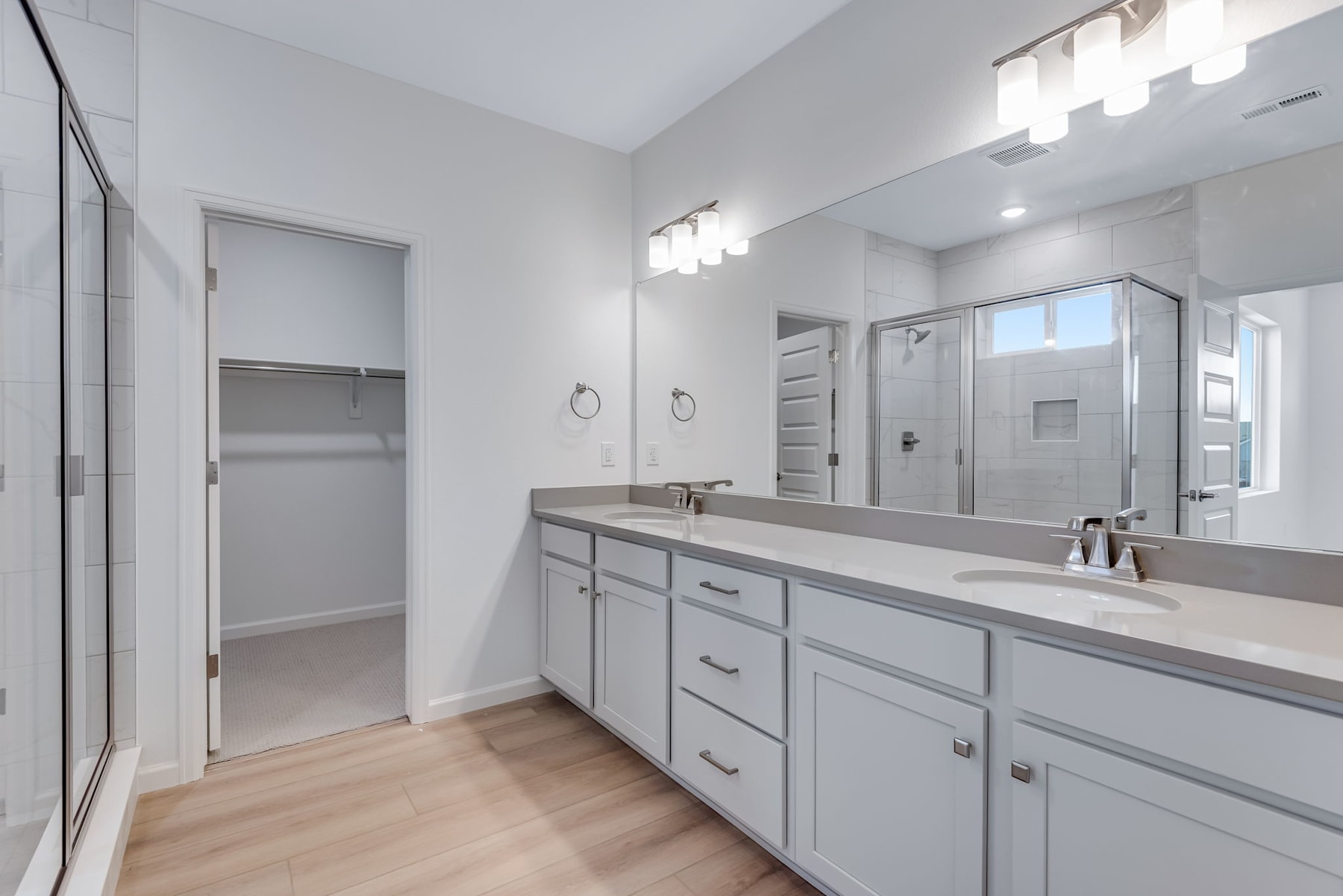 A modern, well-lit bathroom with a double vanity, a large mirror, and a closet door visible in the background.