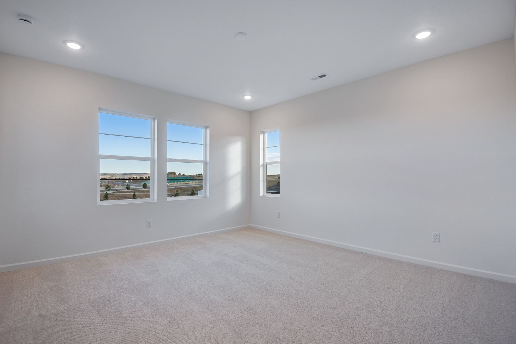 A bright, spacious room with large windows overlooking a scenic outdoor view, featuring hardwood floors and recessed lighting.