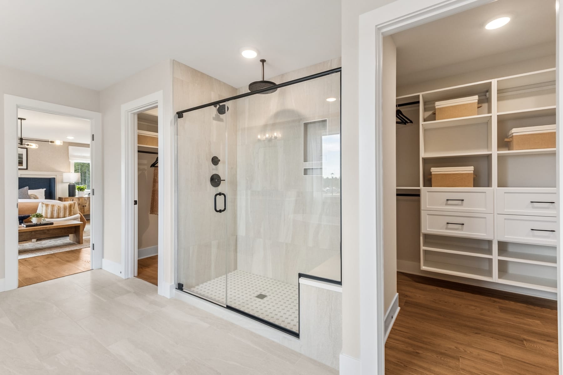 A spacious and well-designed bathroom with a glass-enclosed shower, a built-in closet system, and hardwood flooring, creating a modern and functional living space.