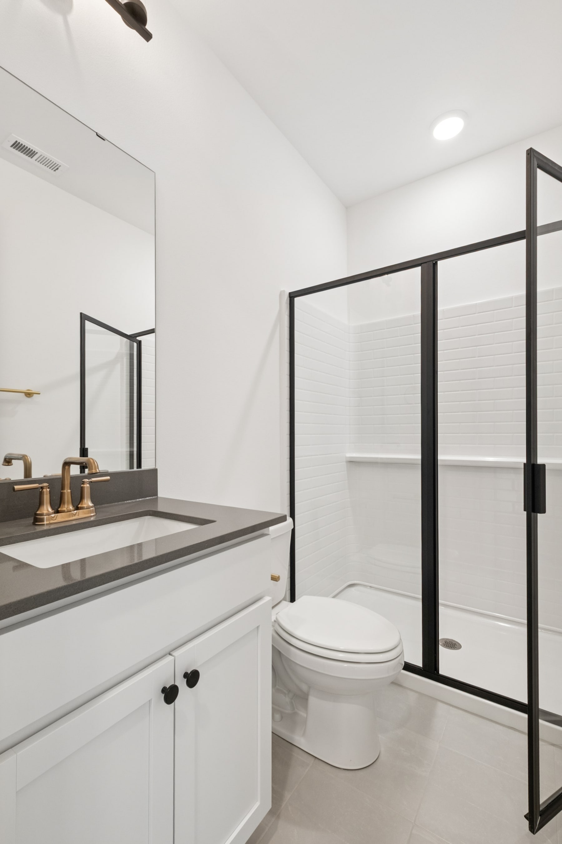 A modern, minimalist bathroom with a white vanity, a toilet, and a black-framed glass shower enclosure.