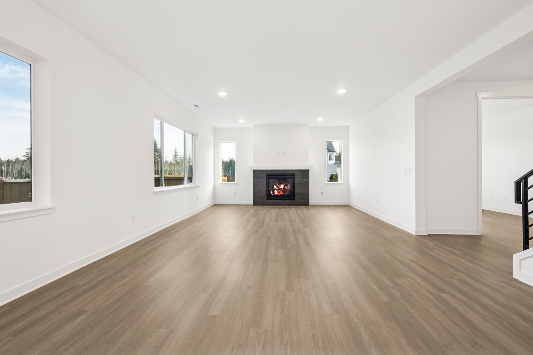 A spacious, minimalist living room with a fireplace, hardwood floors, and large windows overlooking a scenic outdoor landscape.