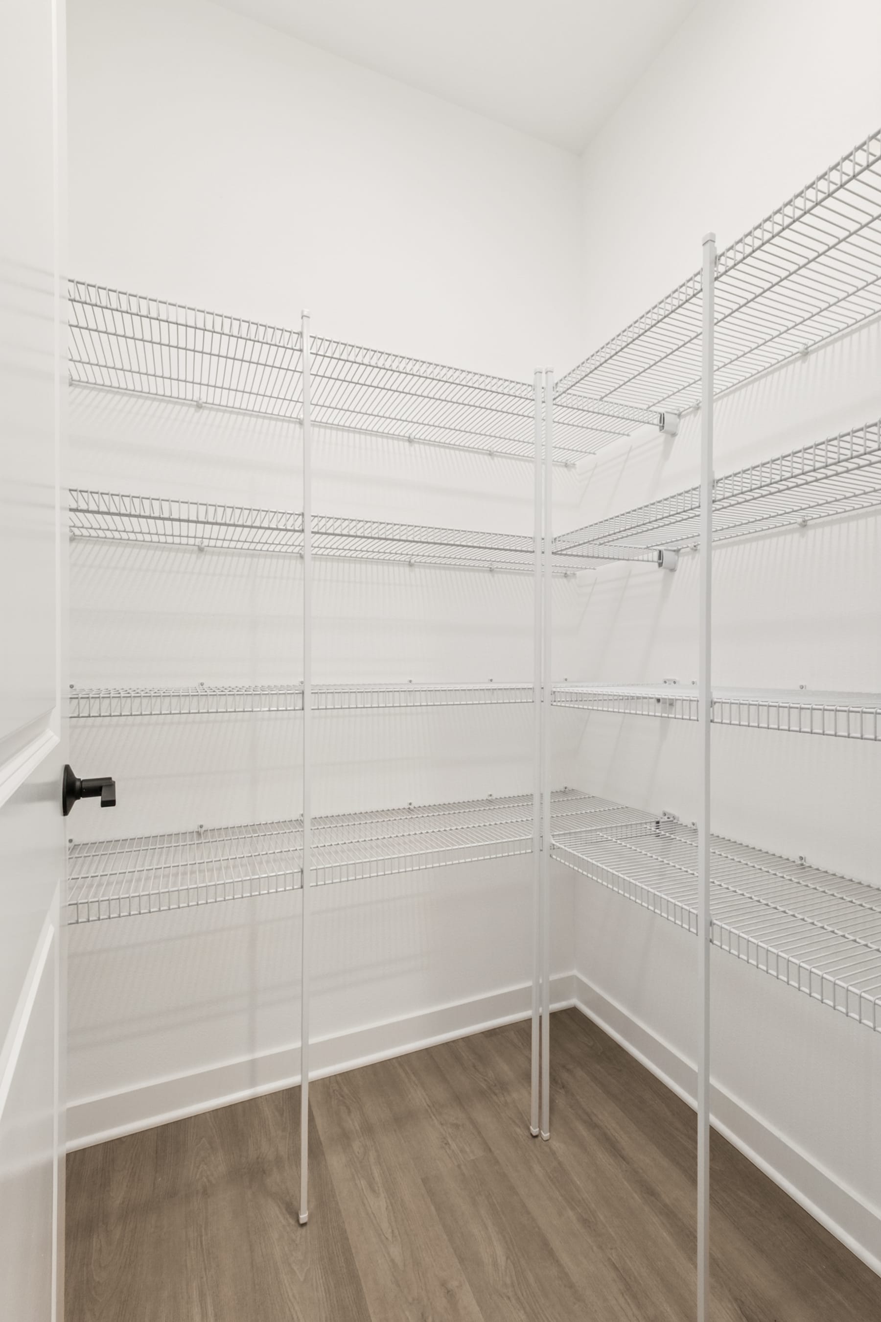 A spacious walk-in closet with white wire shelving units lining the walls, providing ample storage space, and a wooden floor.