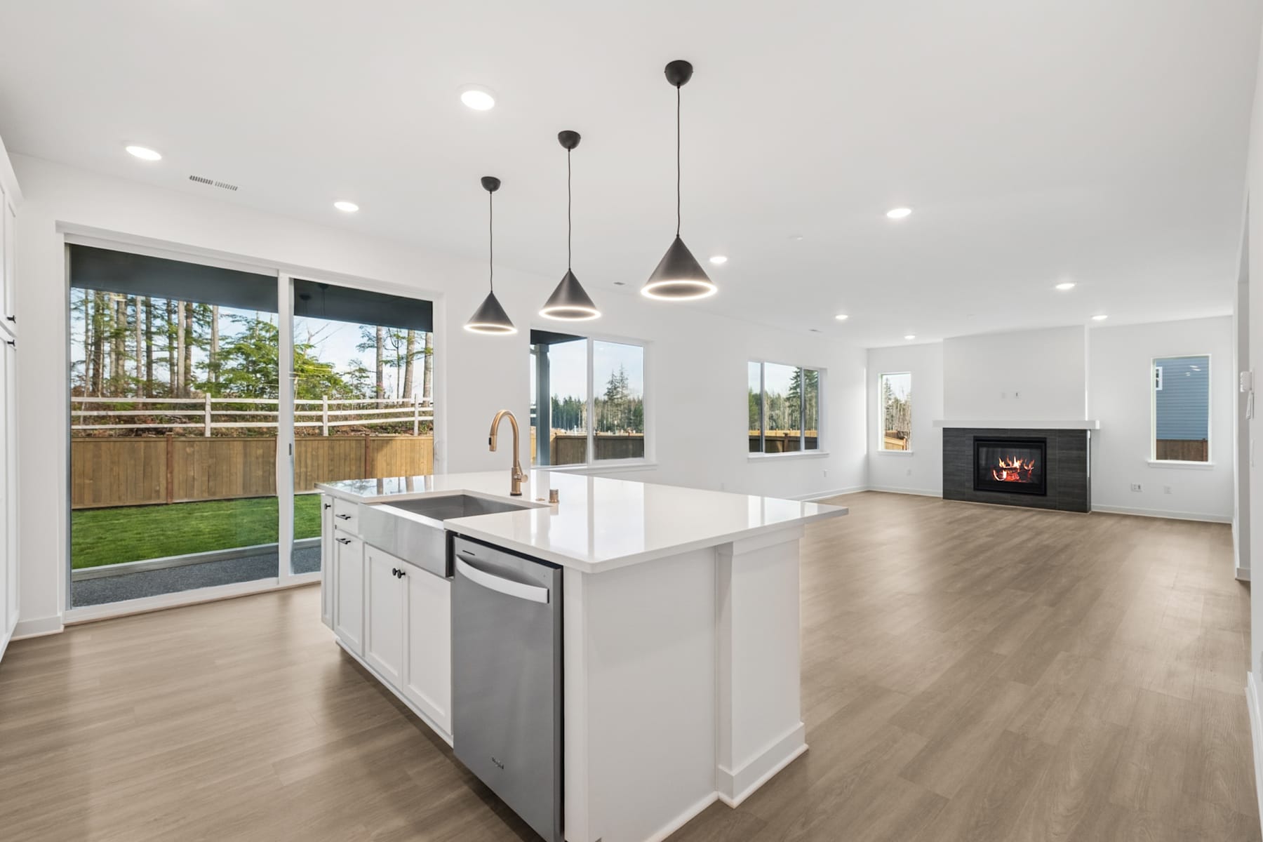 A modern, open-concept kitchen with a large island, pendant lighting, and a view of the backyard through sliding glass doors.