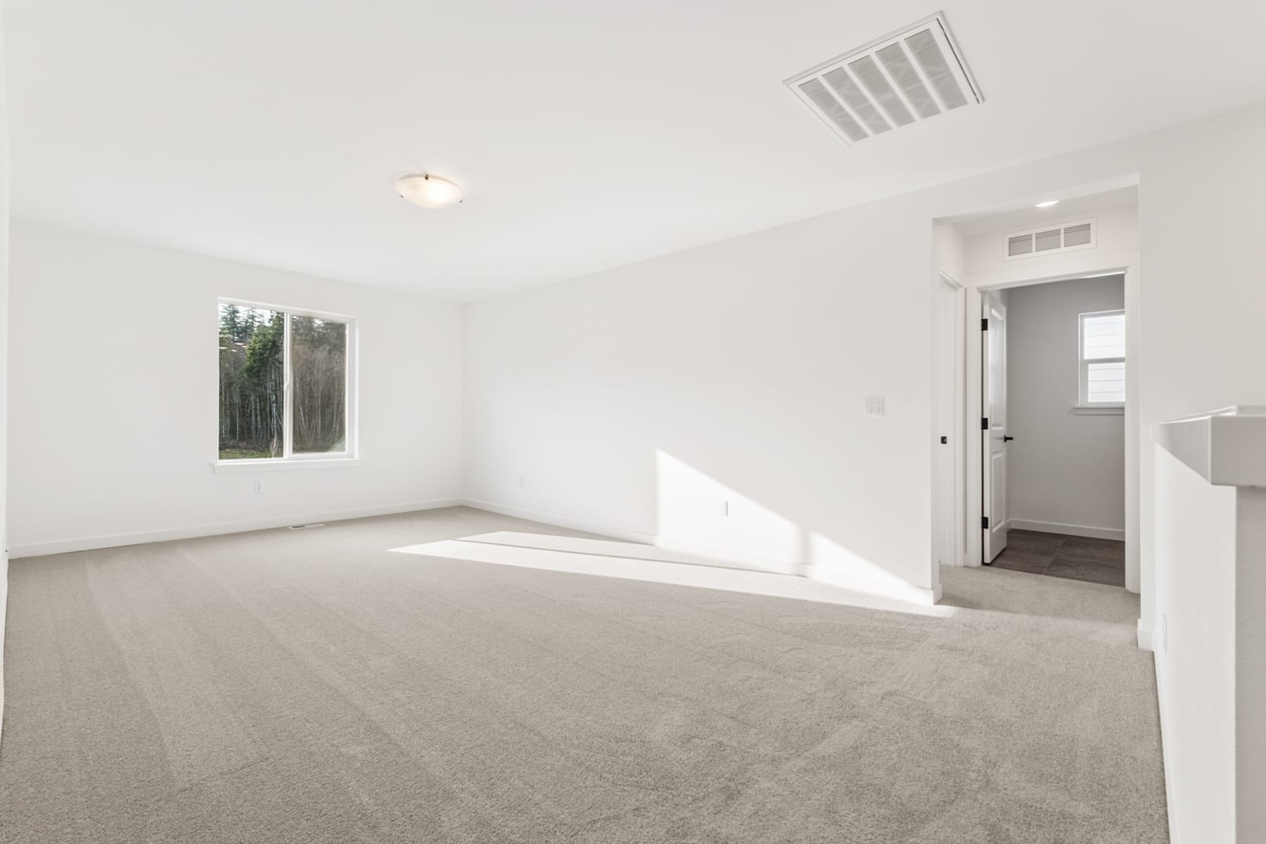 A bright, minimalist room with a large window, hardwood floors, and a doorway leading to another room.
