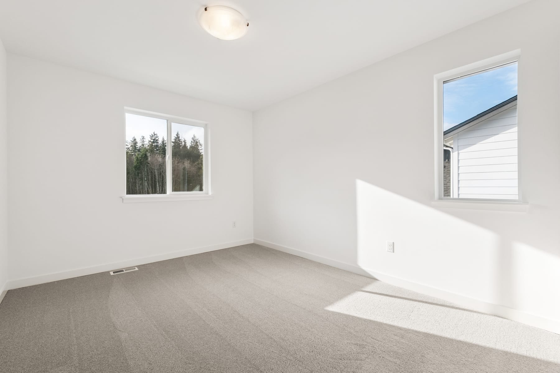 A bright and spacious room with white walls, a carpeted floor, and large windows overlooking a forested landscape.